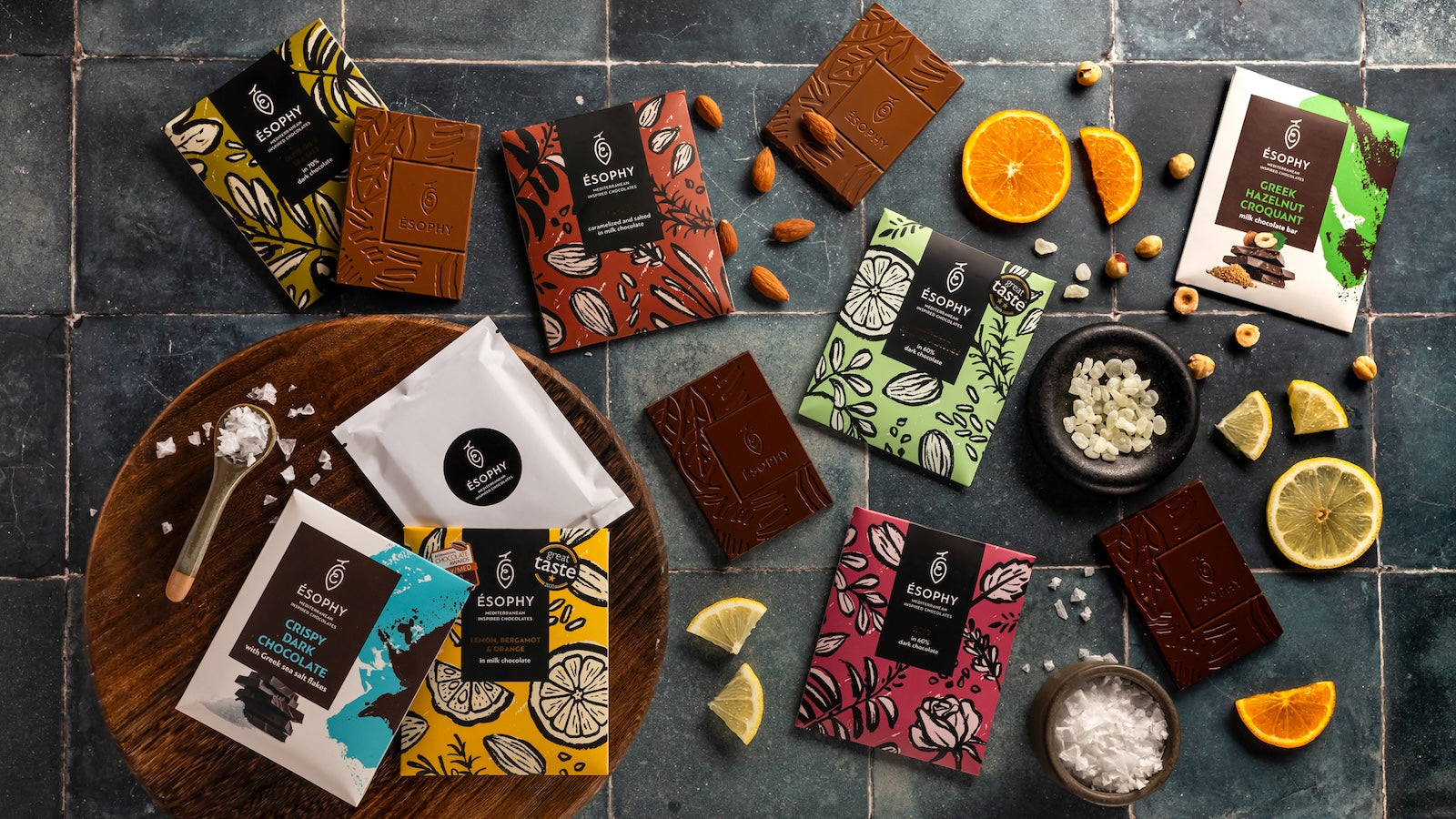 Laconic Foods Greek chocolate collection with assorted Esophy chocolate bars, chocolate pieces, citrus slices, almonds, hazelnuts, and sea salt.
