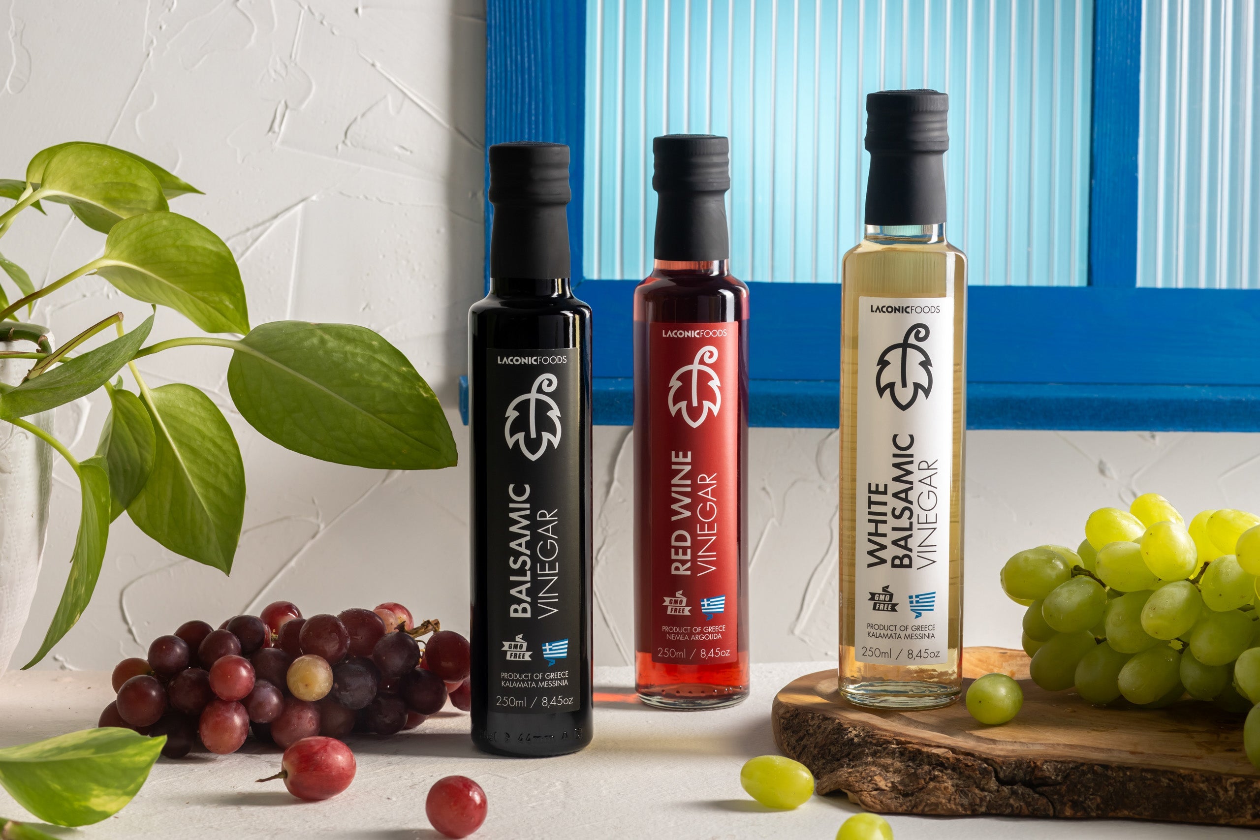 Bottles of Laconic Foods Greek Balsamic and Red Wine Vinegar (250ml) with fresh vegetables and herbs