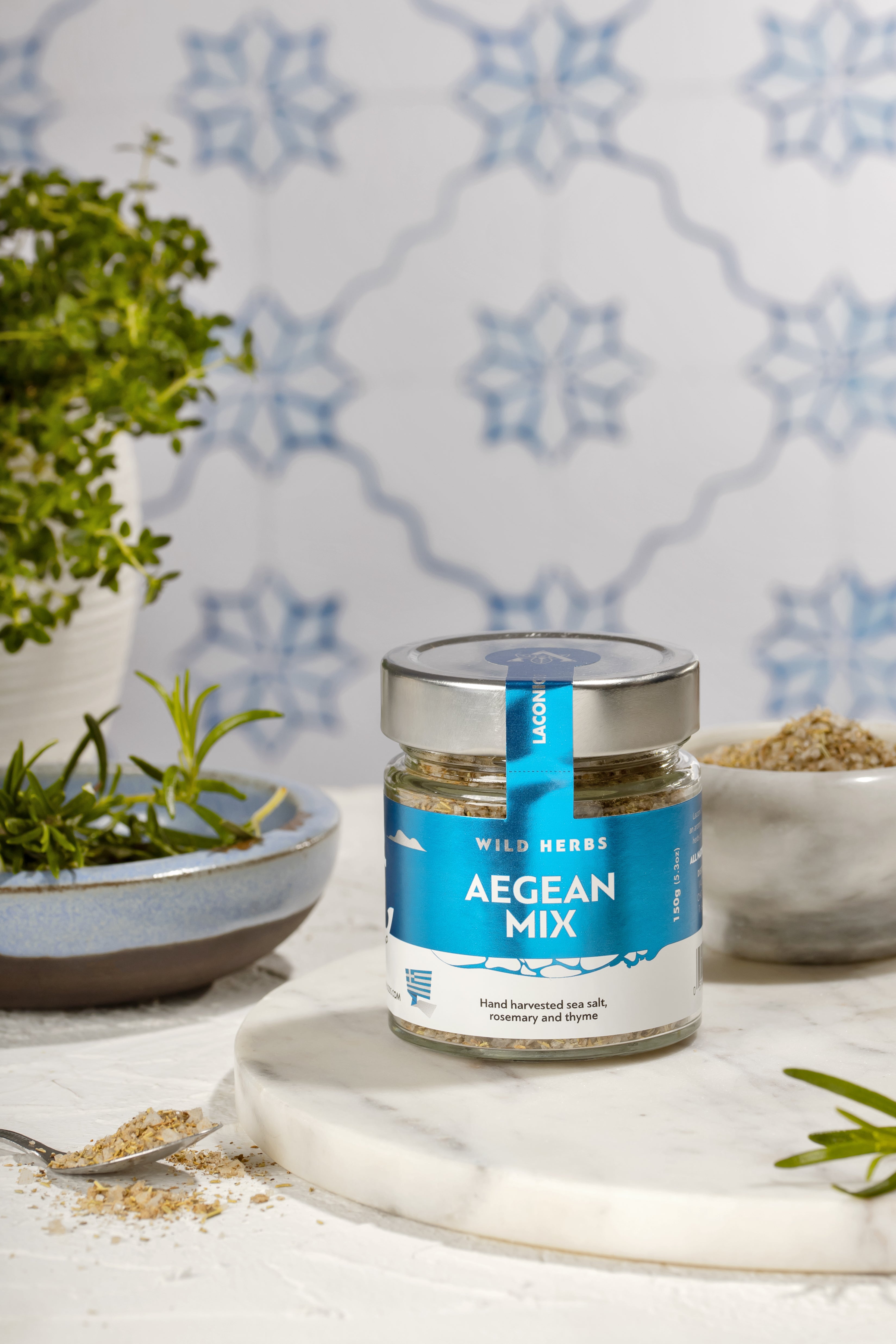 Laconic Foods Aegean Mix spice jar with sea salt, rosemary, and thyme on marble counter with fresh herbs
