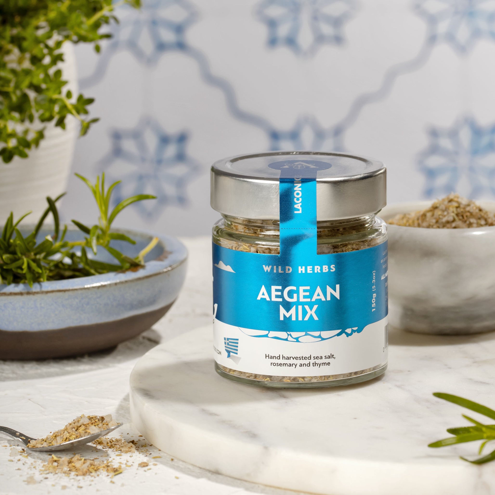 Laconic Foods Aegean Mix spice jar with sea salt, rosemary, and thyme on marble counter with fresh herbs