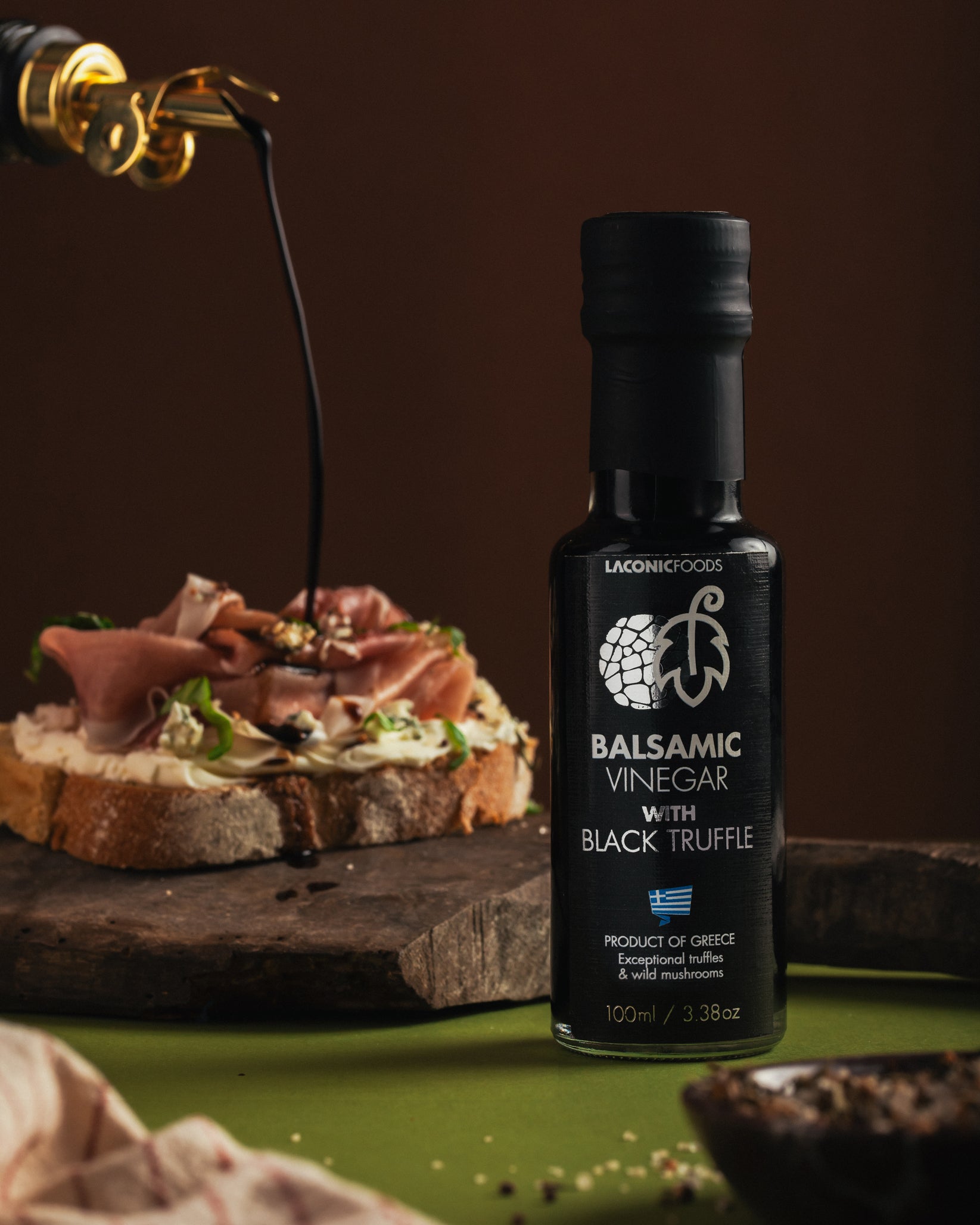 Laconic Foods Balsamic Vinegar with Black Truffle displayed on a rustic board with balsamic being poured over artisan bread.