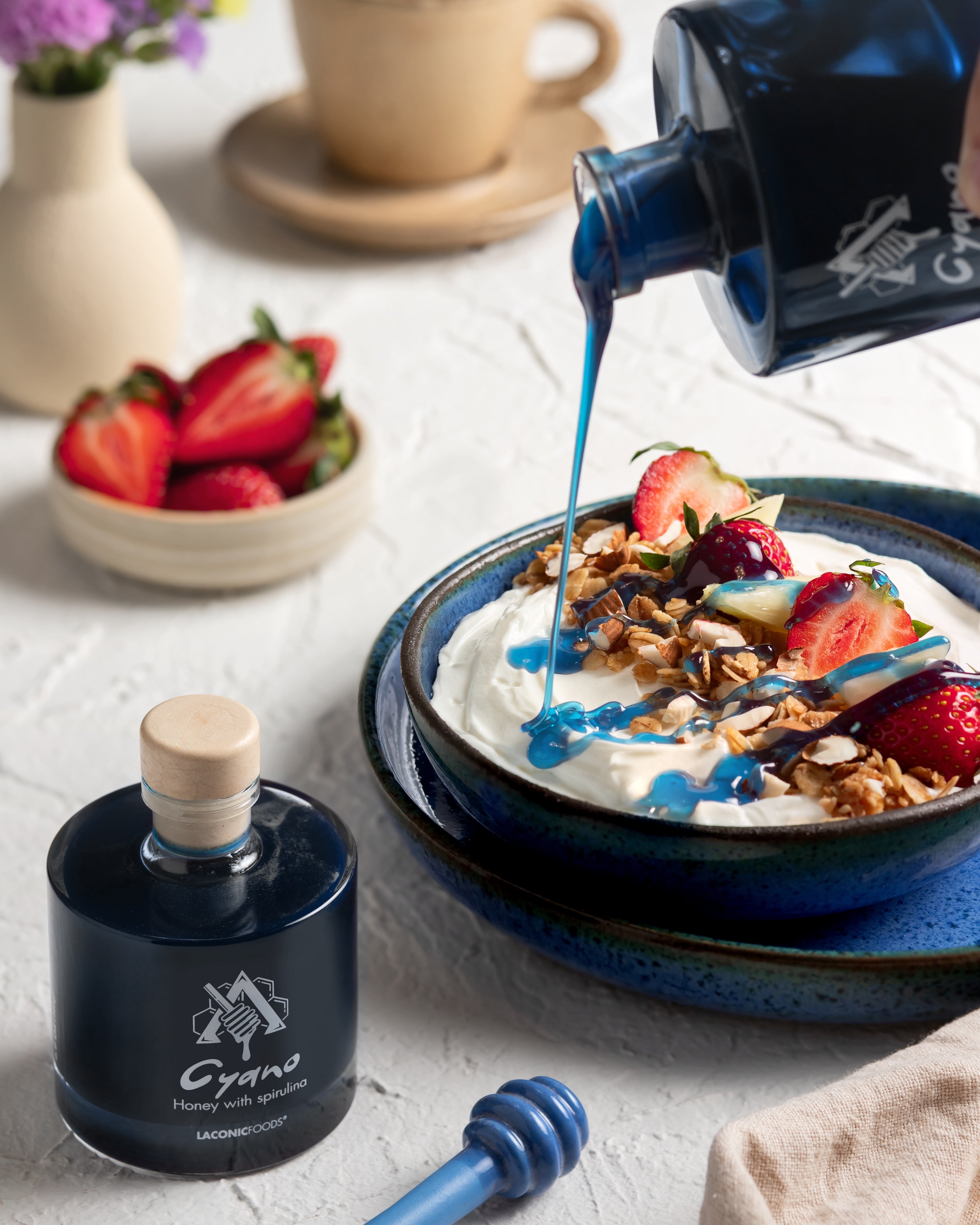 Cyano blue honey with spirulina poured over Greek yogurt, granola, and strawberries — Laconic Foods artisanal Greek honey.