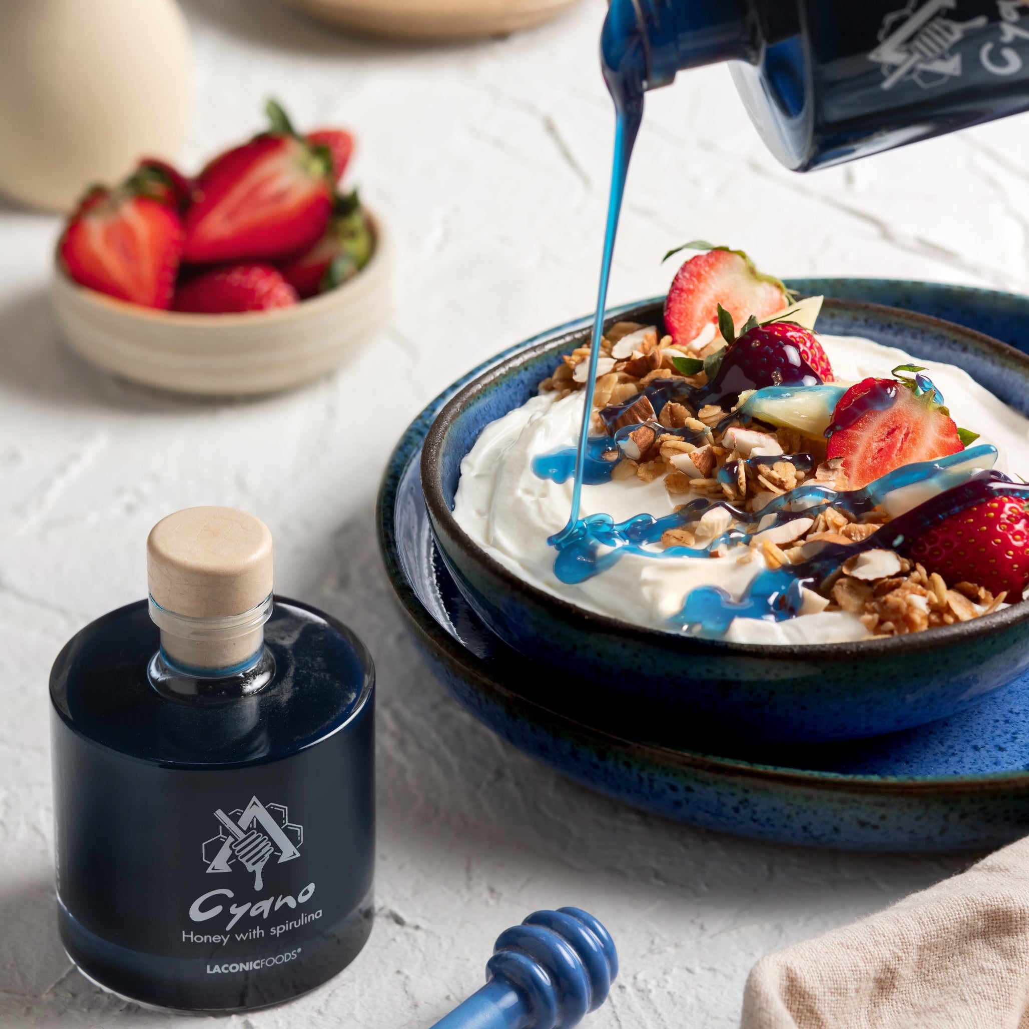Cyano blue honey with spirulina poured over Greek yogurt, granola, and strawberries — Laconic Foods artisanal Greek honey.