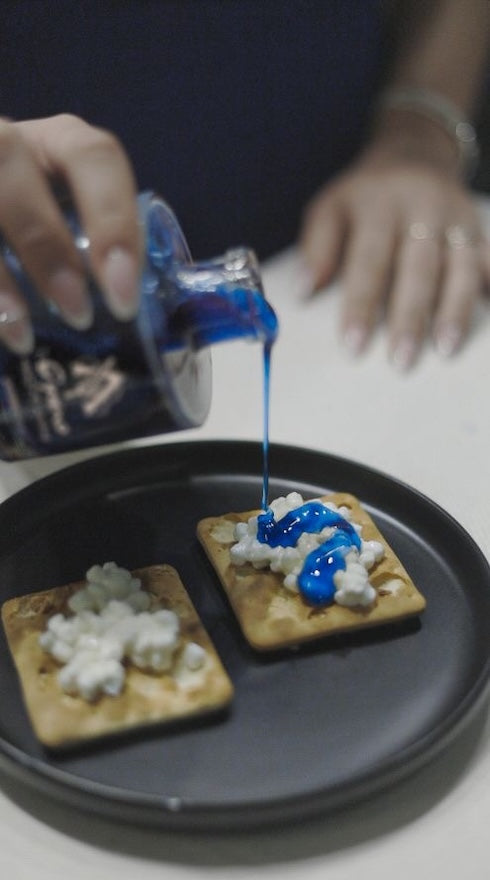 Cyano blue honey with spirulina drizzled on crackers topped with soft cheese — elegant serving idea from Laconic Foods.