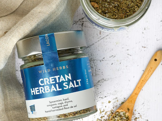 Overhead view of Laconic Foods Cretan Herbal Salt with wild Greek herbs and fleur de sel, shown with rustic wooden spoon and open jar