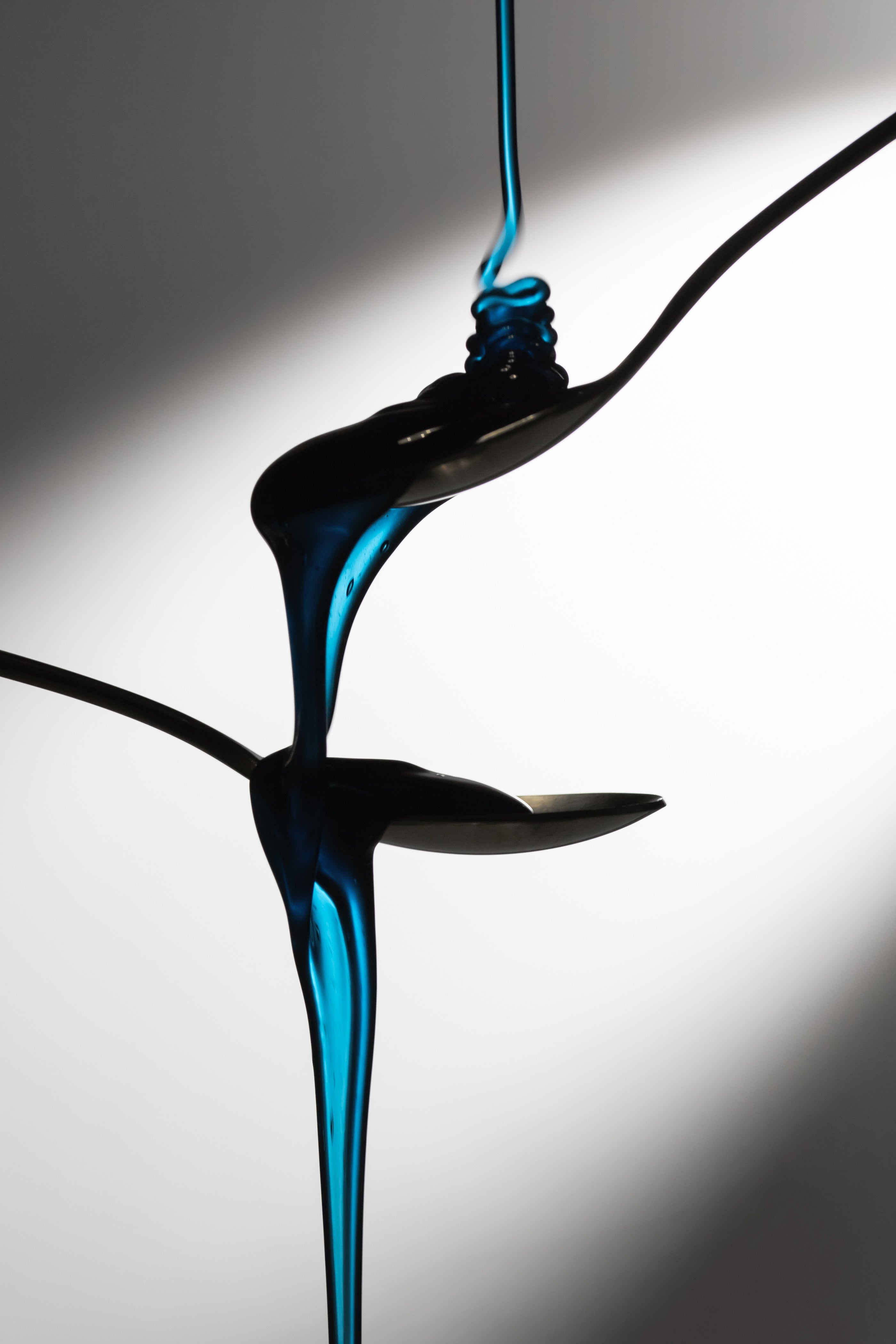 Dramatic pour of Cyano blue honey with spirulina over stacked spoons, highlighting the deep blue tone.