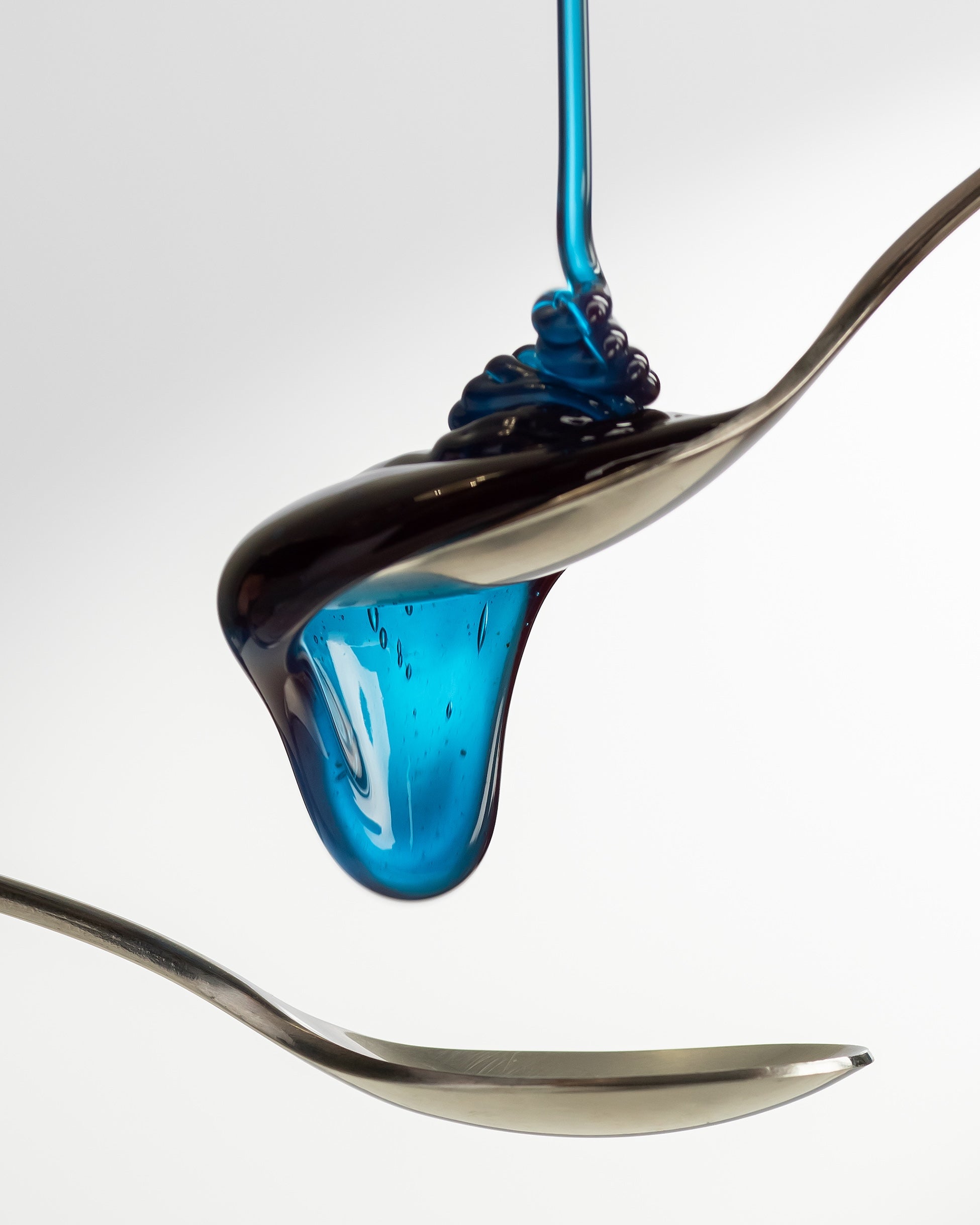 Macro shot of Cyano blue honey with spirulina forming a glossy drop between two spoons.