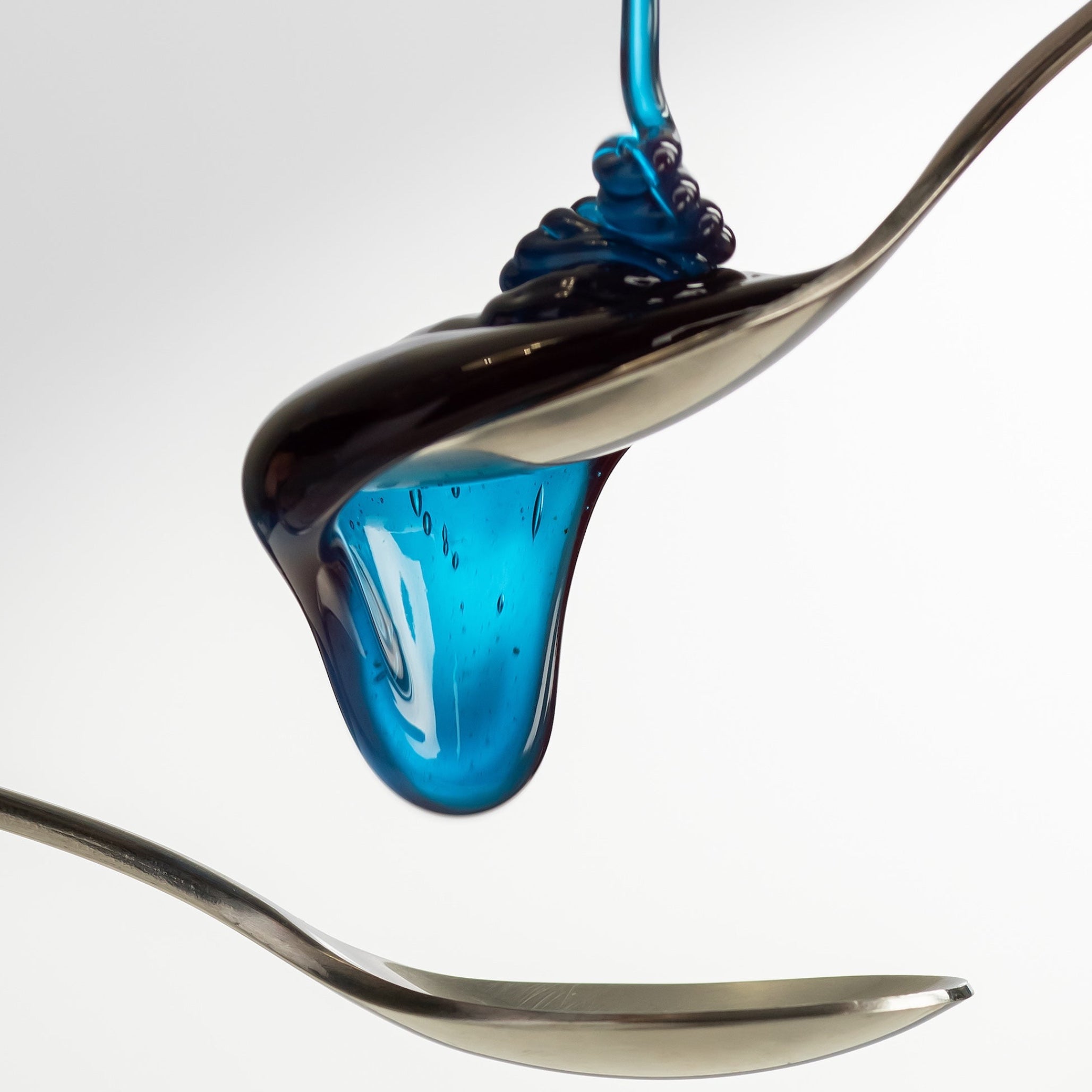 Macro shot of Cyano blue honey with spirulina forming a glossy drop between two spoons.