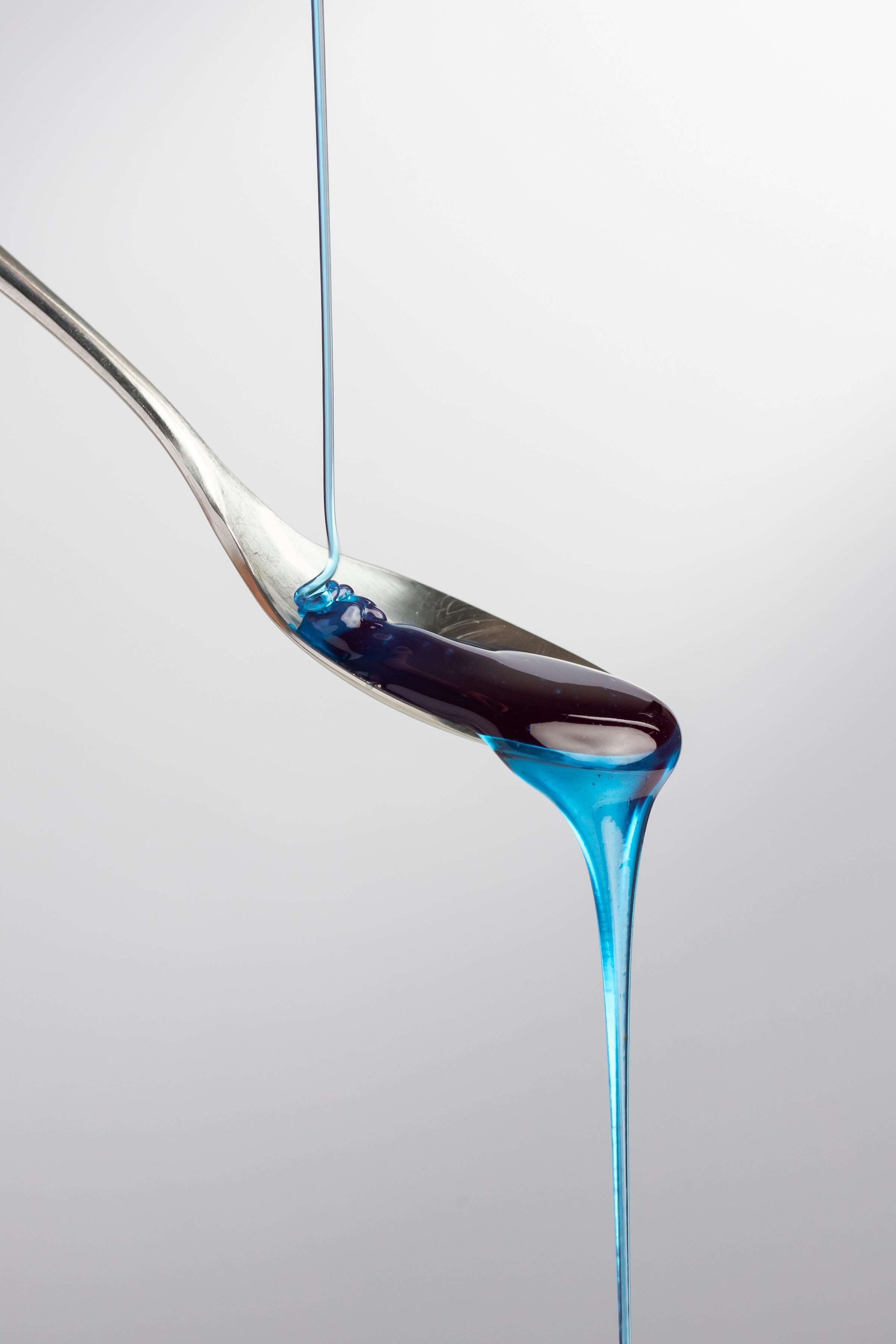 Thin stream of Cyano blue honey with spirulina flowing onto a silver spoon, showcasing clarity and viscosity.
