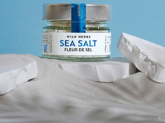 Fleur de Sel Greek sea salt by Laconic Foods on Mediterranean sand with blue background