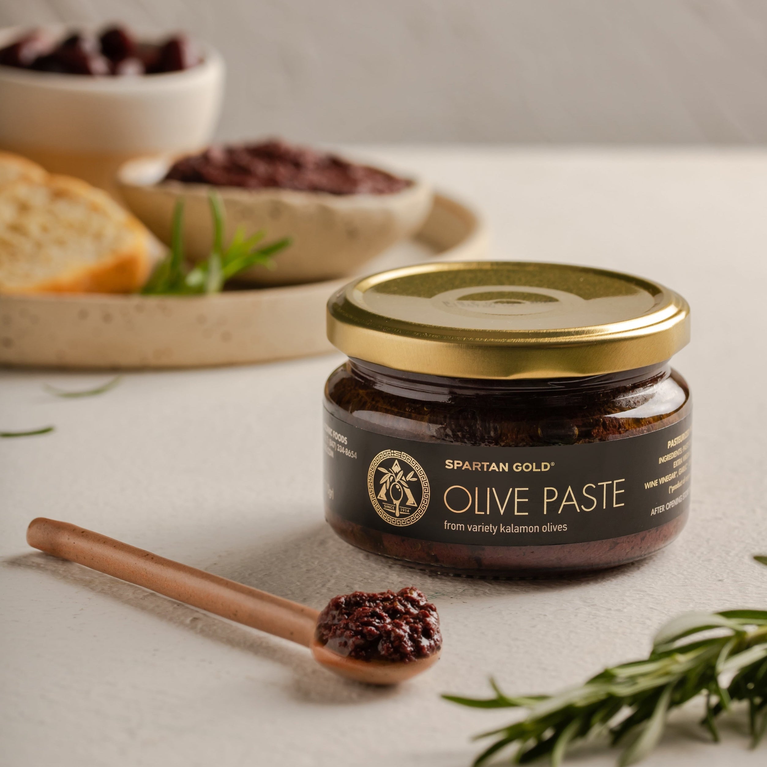 Artisan Greek Kalamata Olive Paste with olive oil, bread, and rosemary on counter