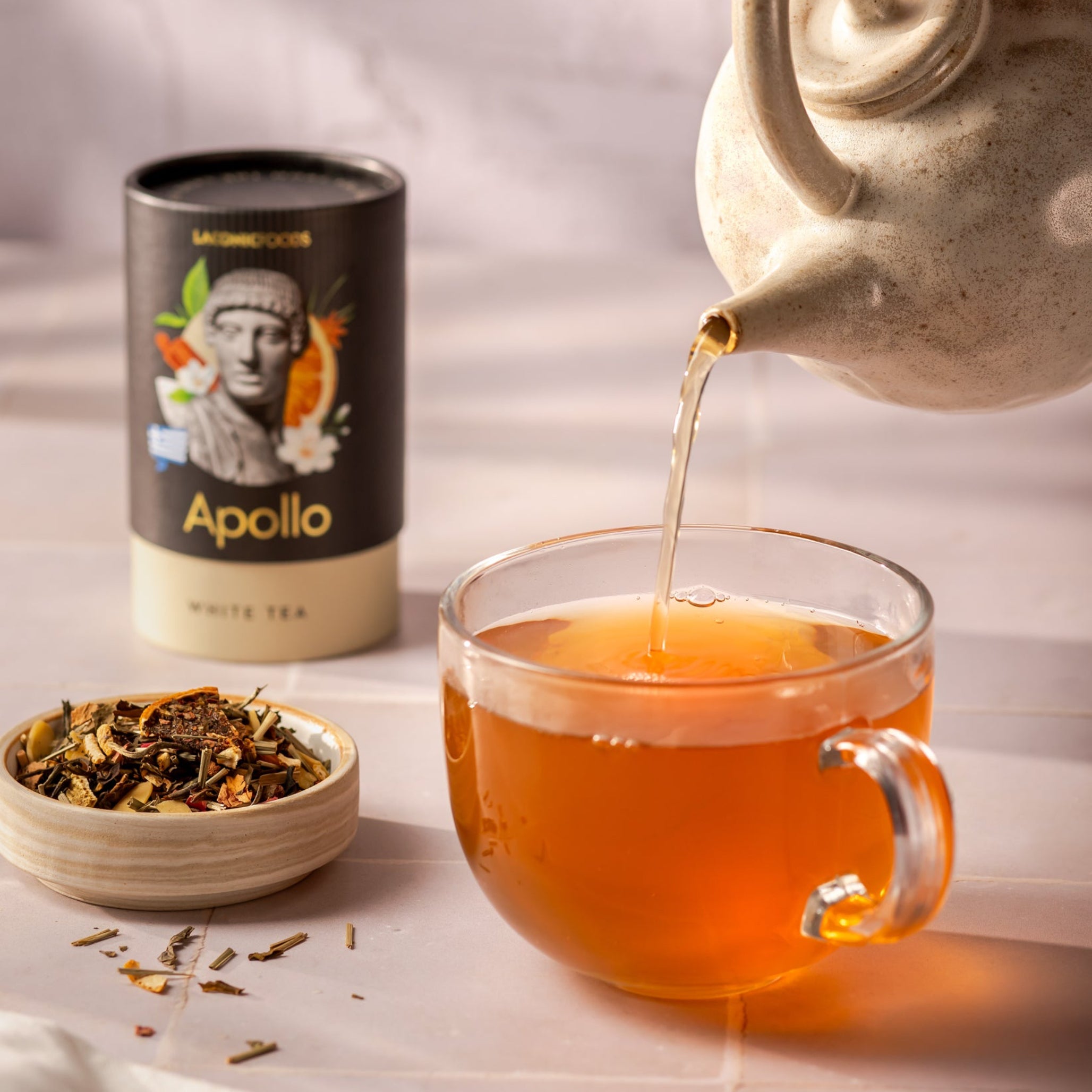 Laconic Foods Apollo White Tea poured into glass cup from ceramic teapot β Greek white tea with citrus and floral notes.