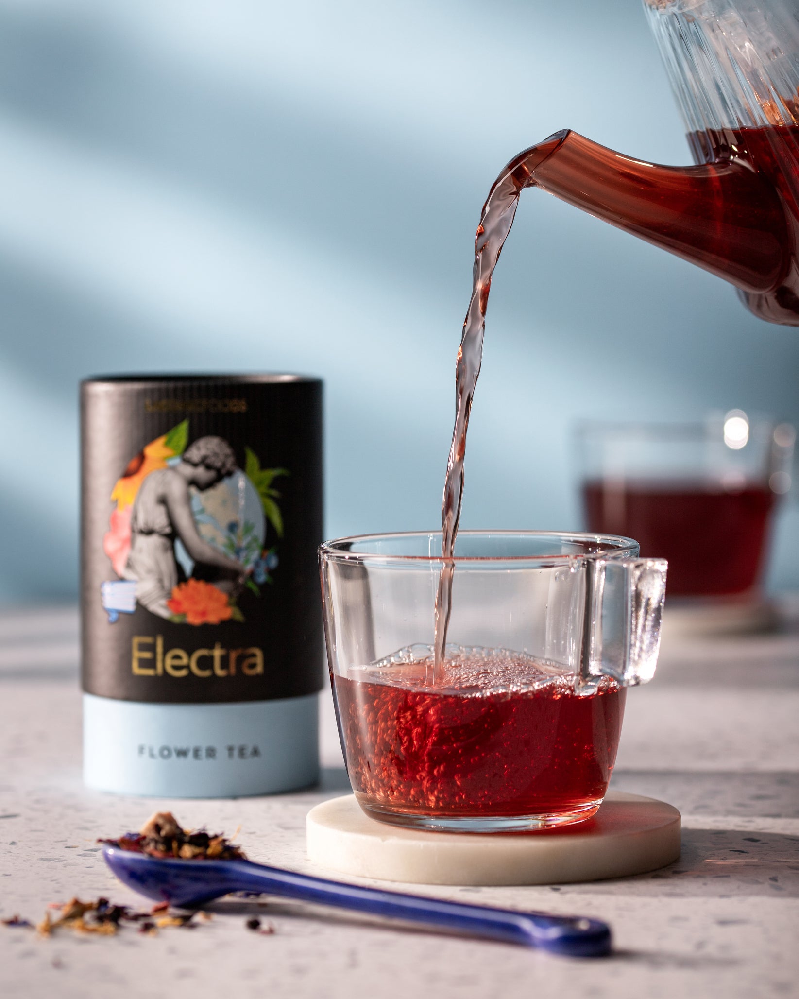Laconic Foods Electra Flower Tea poured into glass cup with vivid red infusion – elegant Greek loose leaf tea with floral aroma.