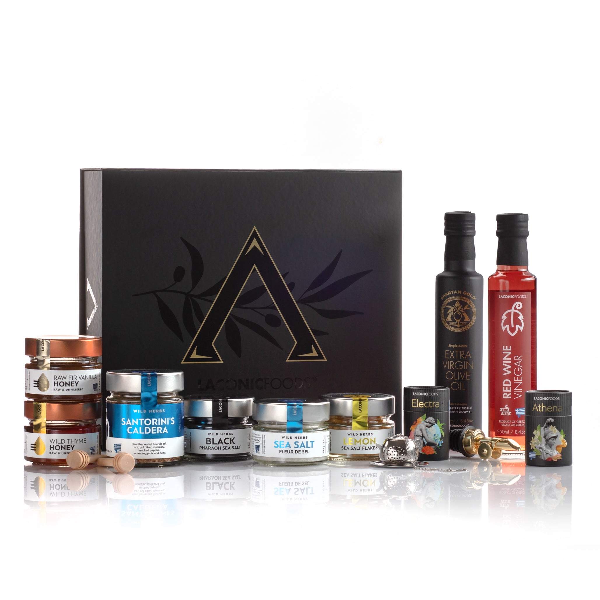 Full product display of the Laconic Foods Luxury Greek Gift Box contents arranged outside the box, including olive oil, red wine vinegar, sea salts, honeys, Santorini spice mix, mini teas, honey dippers, and accessories.