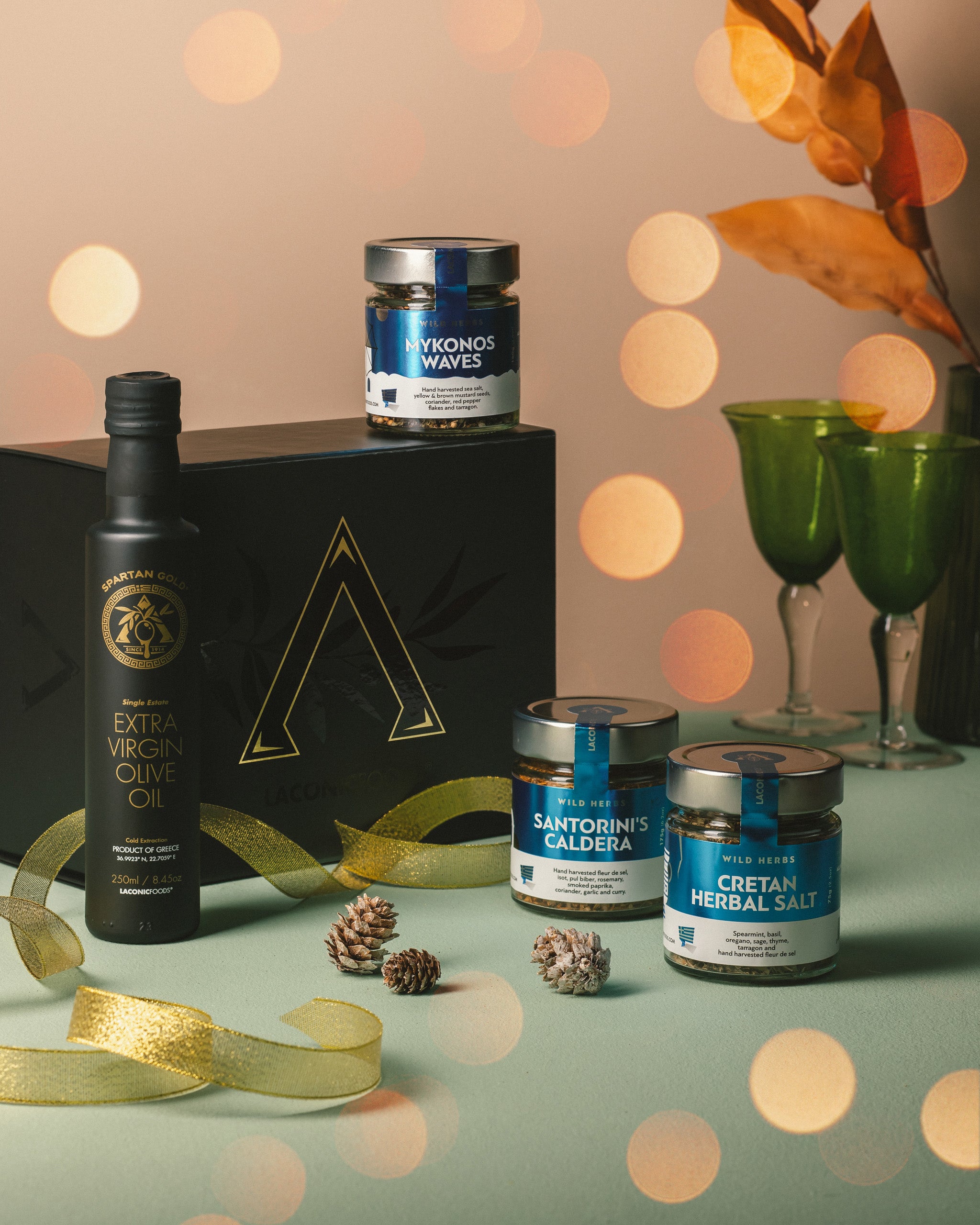 Festive holiday display of Laconic Foods Greek gift box with extra virgin olive oil and three herbal spice blends, styled with ribbon and pinecones.