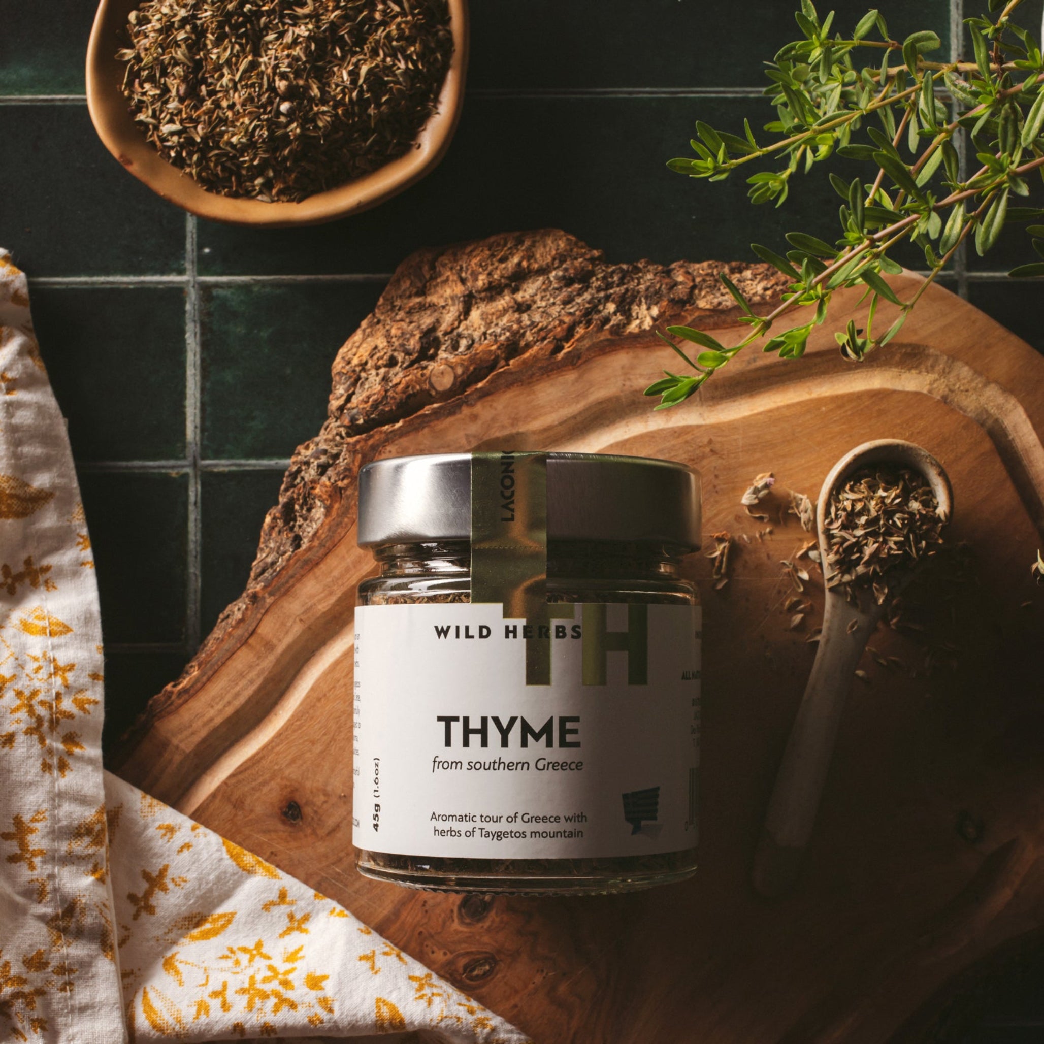 Laconic Foods Greek thyme wild herbs in a glass jar on a wooden board with dried thyme and fresh herbs.