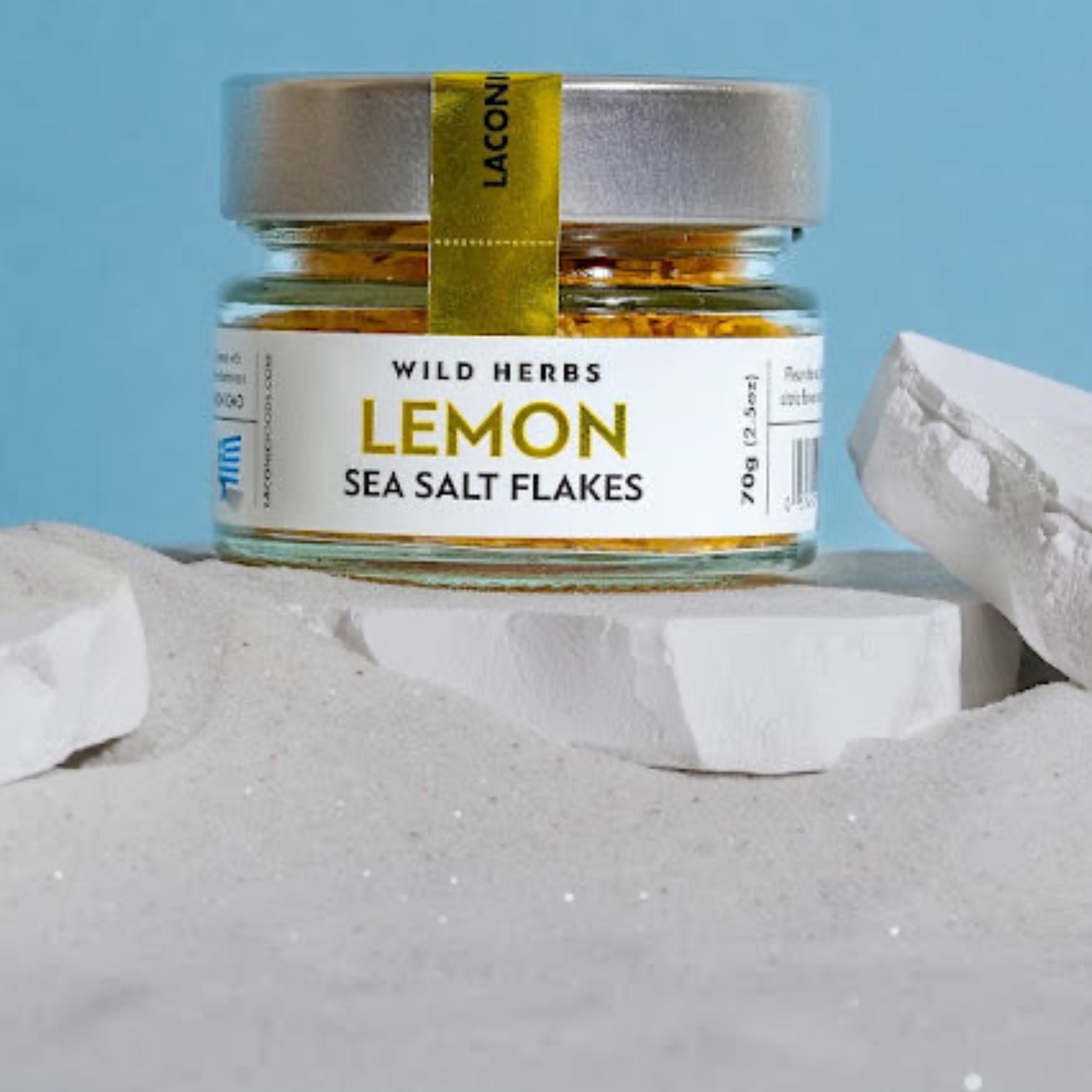 Lemon Sea Salt Flakes 70g jar by Laconic Foods displayed in white sand with blue background