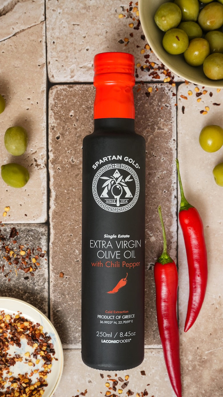 Overhead shot of chili olive oil bottle with red chili peppers, crushed chili flakes, and green olives