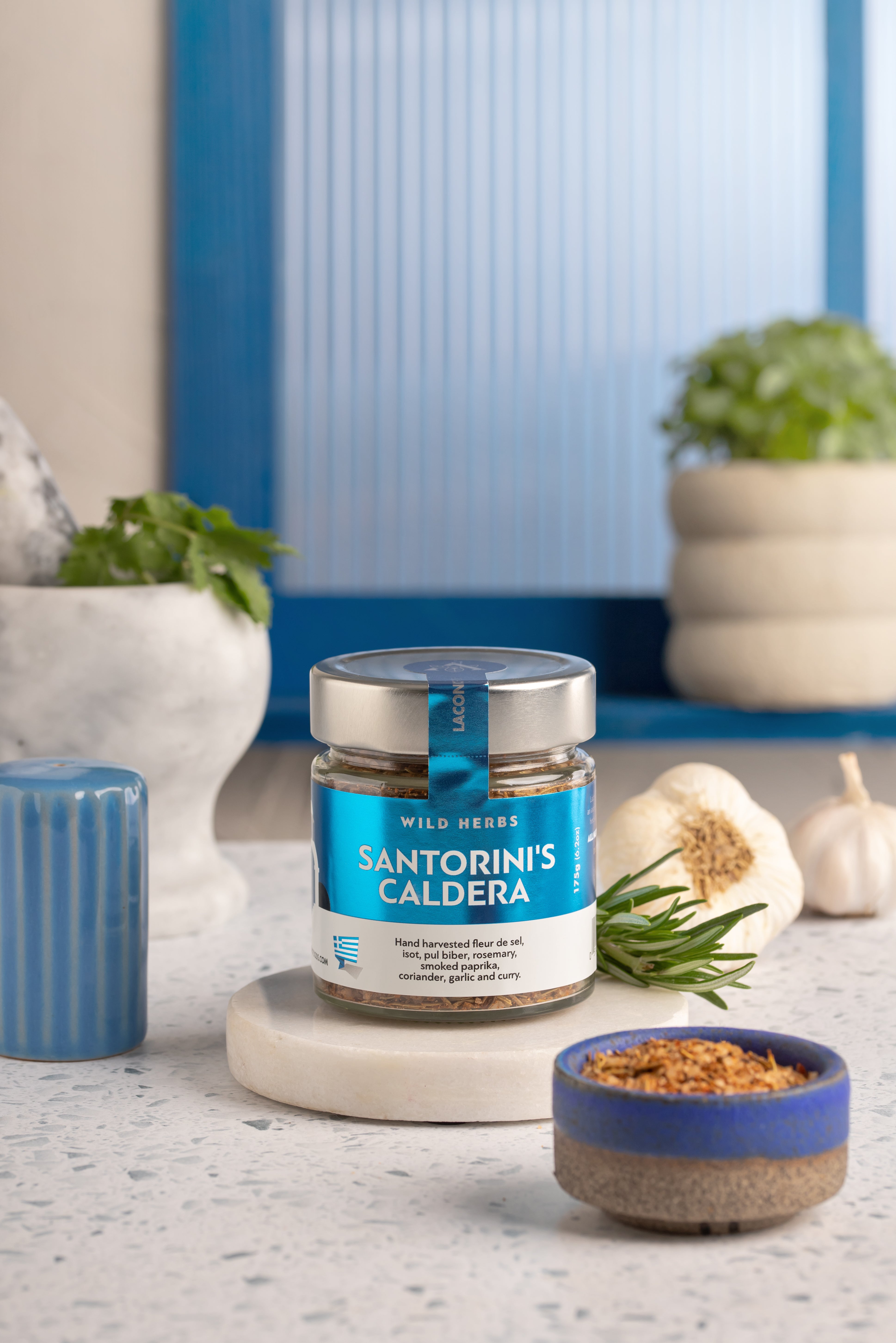Santorini's Caldera spice jar styled on a countertop with rosemary, garlic, and a marble mortar – Mediterranean kitchen background