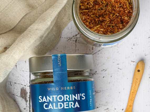 Overhead view of Santorini's Caldera spice jar with visible herbs and wooden spoon on rustic background