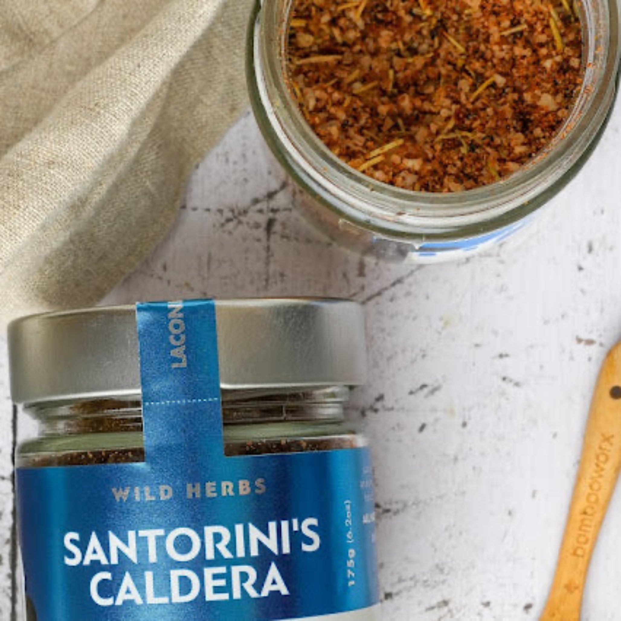 Overhead view of Santorini's Caldera spice jar with visible herbs and wooden spoon on rustic background