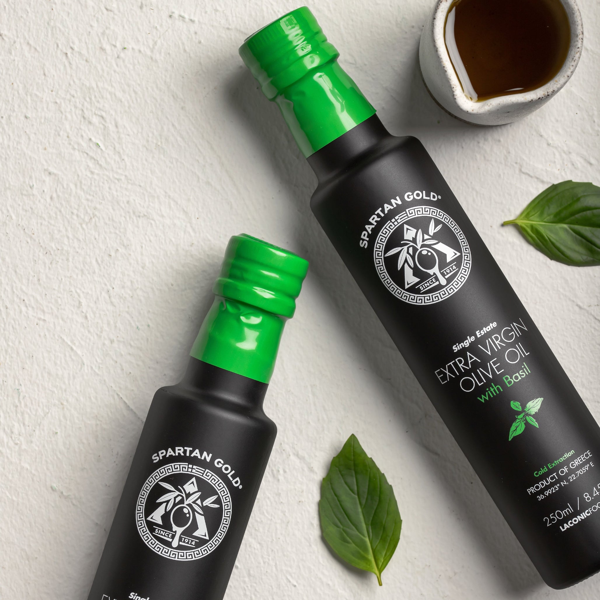 Flat lay of Basil Infused Extra Virgin Olive Oil bottles with fresh basil leaves and olive oil