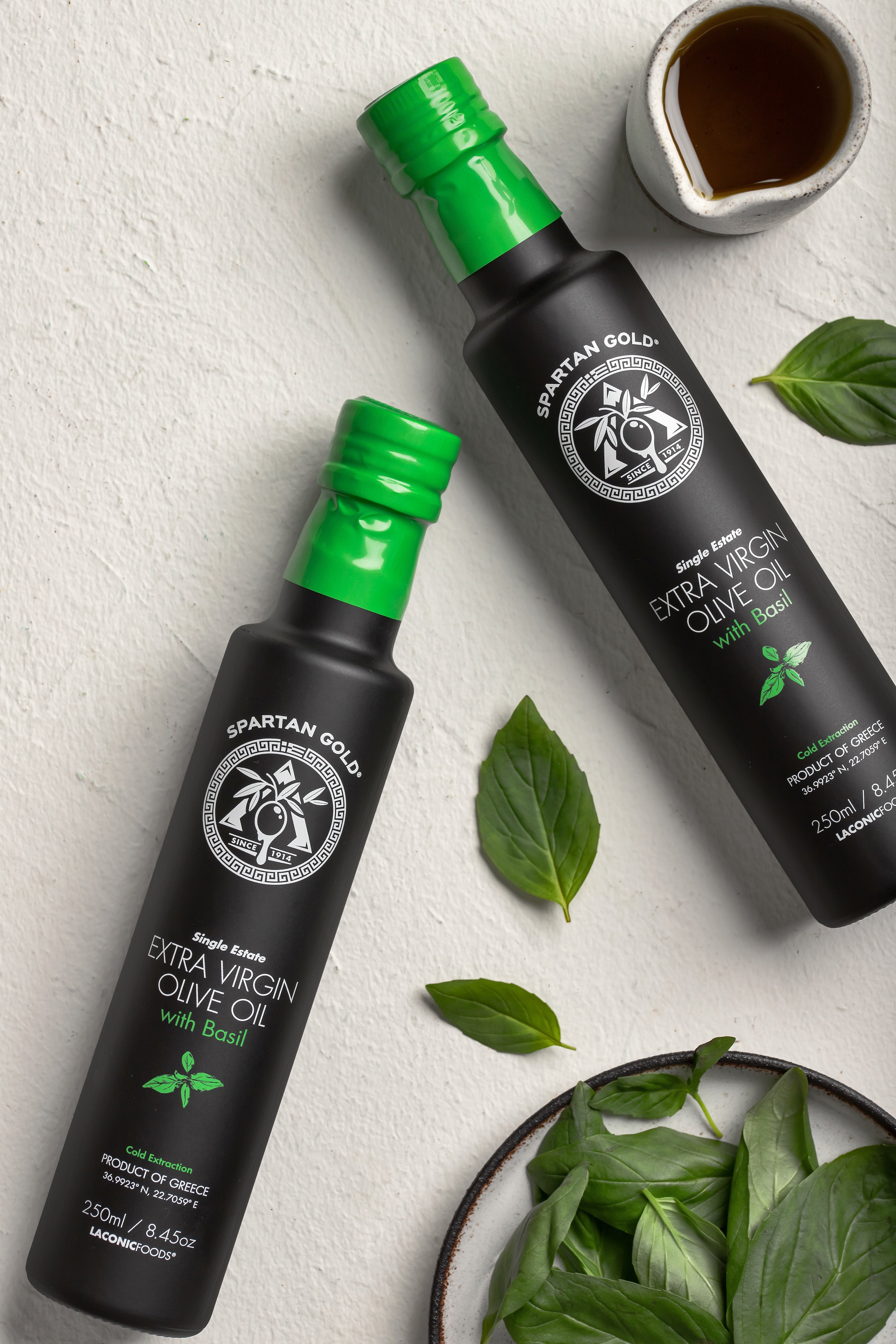 Flat lay of Basil Infused Extra Virgin Olive Oil bottles with fresh basil leaves and olive oil