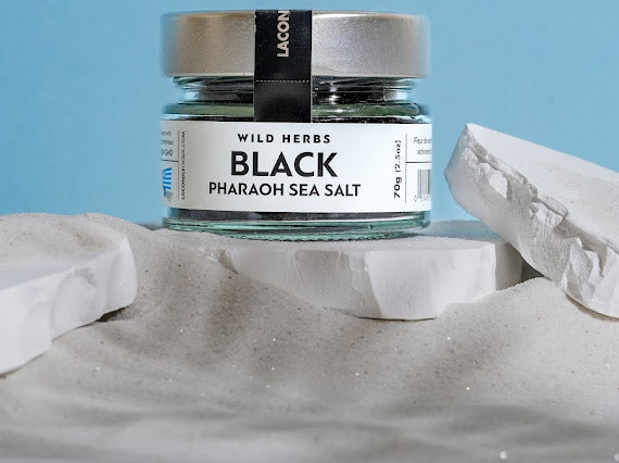 Black Pharaoh Sea Salt 70g jar displayed in white sand with blue background