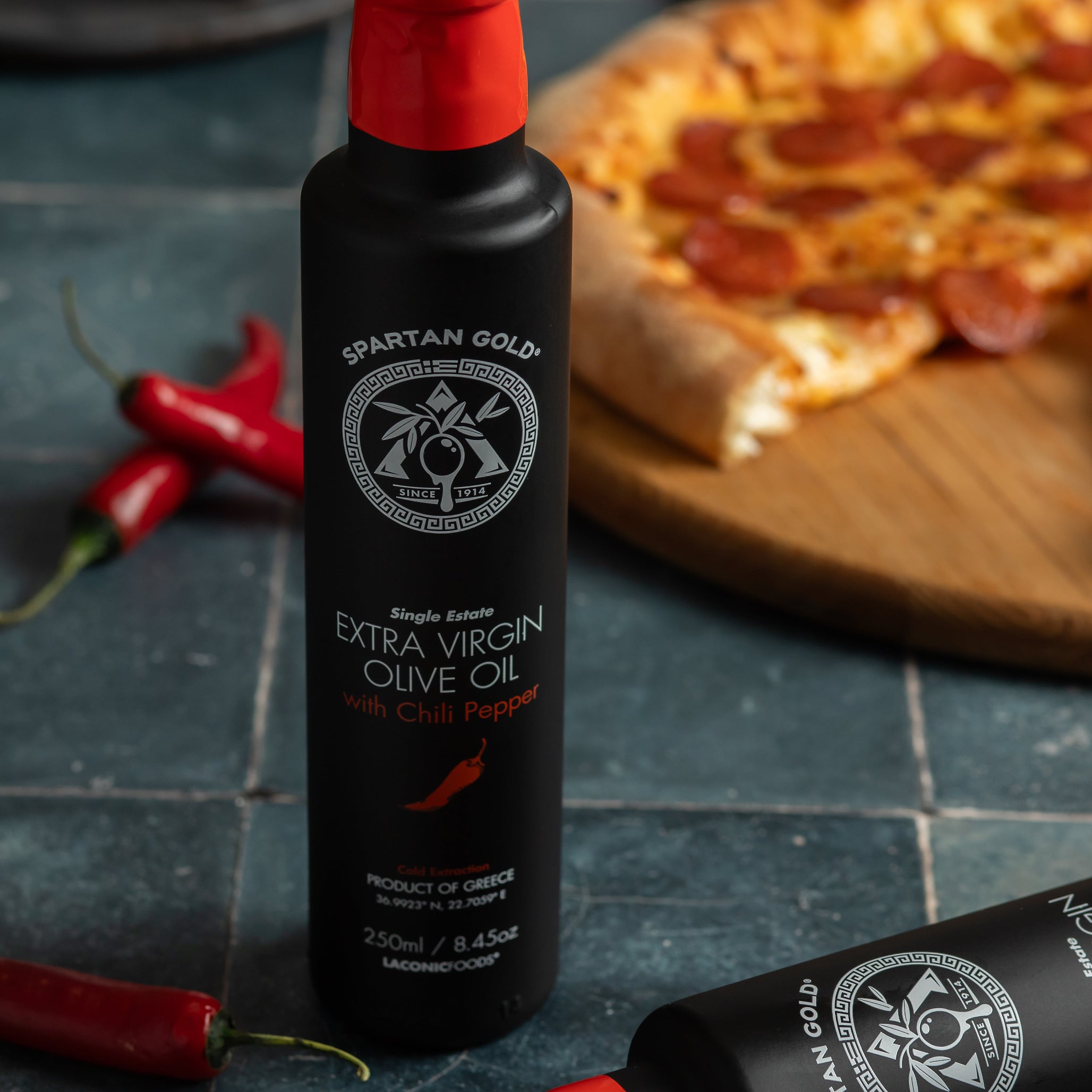 Chili olive oil bottle next to pepperoni pizza and red chili peppers on a dark stone background