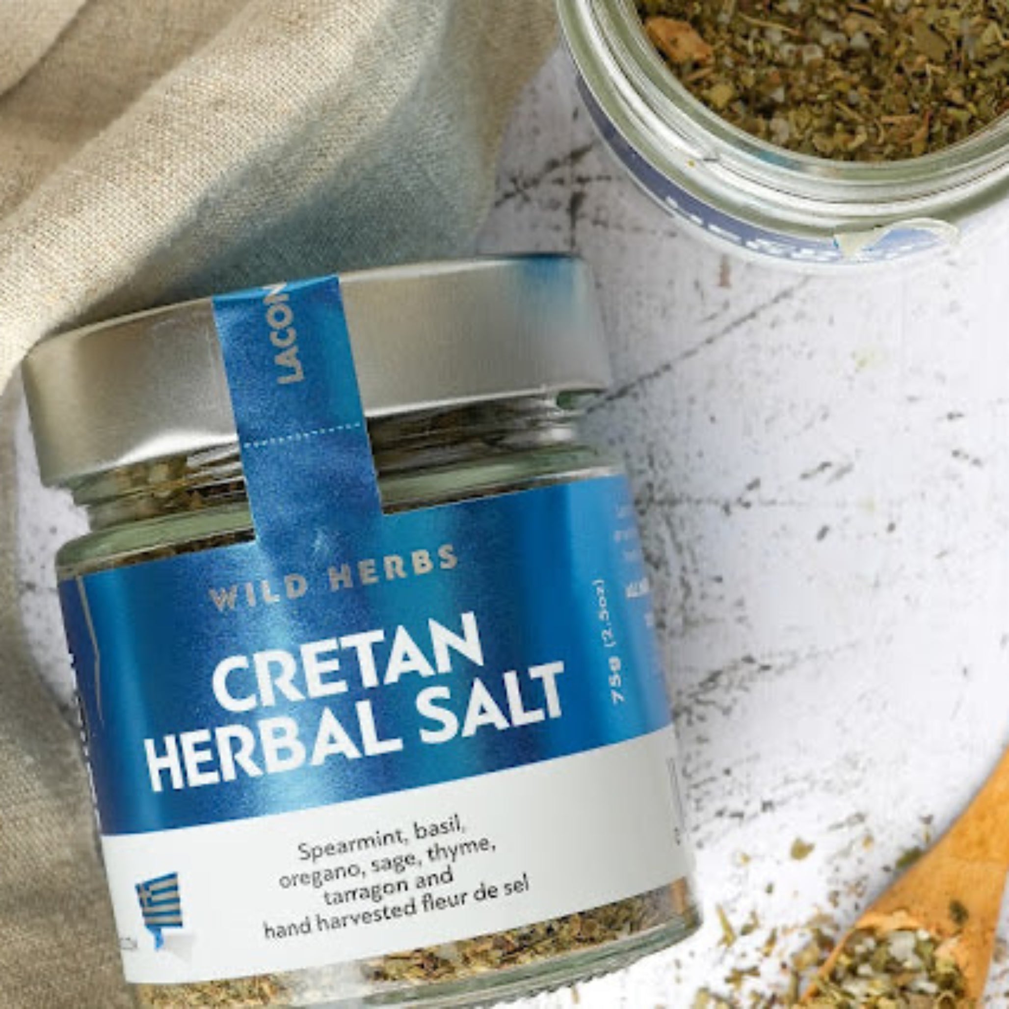 Overhead view of Laconic Foods Cretan Herbal Salt with wild Greek herbs and fleur de sel, shown with rustic wooden spoon and open jar