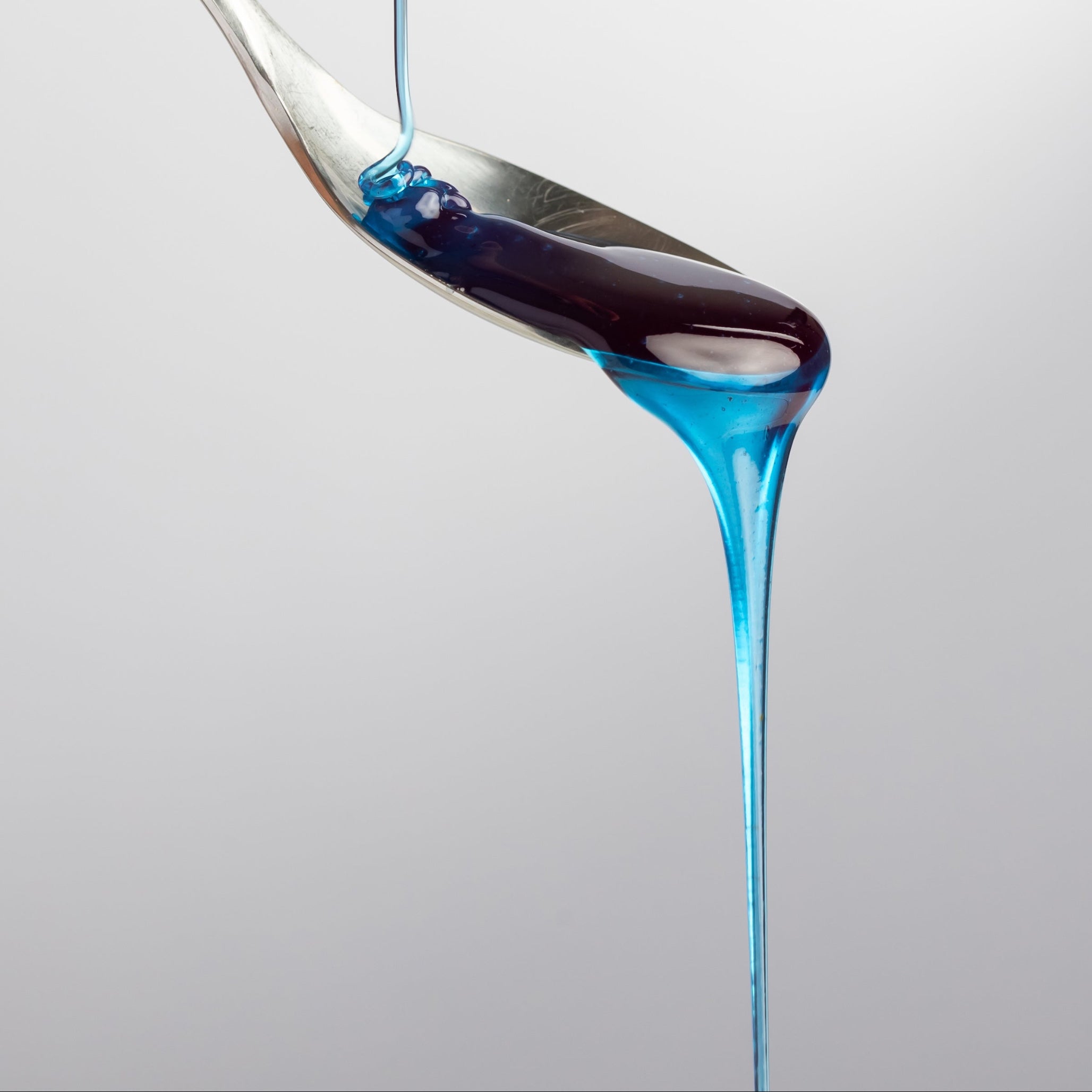 Thin stream of Cyano blue honey with spirulina flowing onto a silver spoon, showcasing clarity and viscosity.