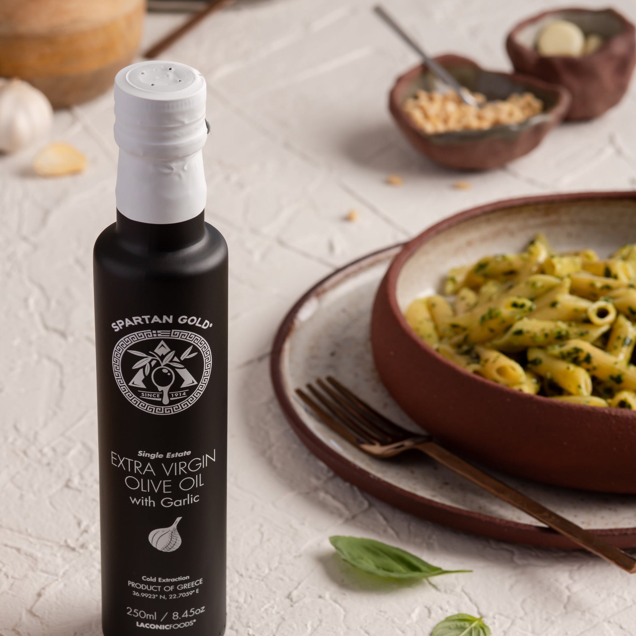 Garlic EVOO bottle next to a bowl of pasta with basil, showcasing Mediterranean cooking