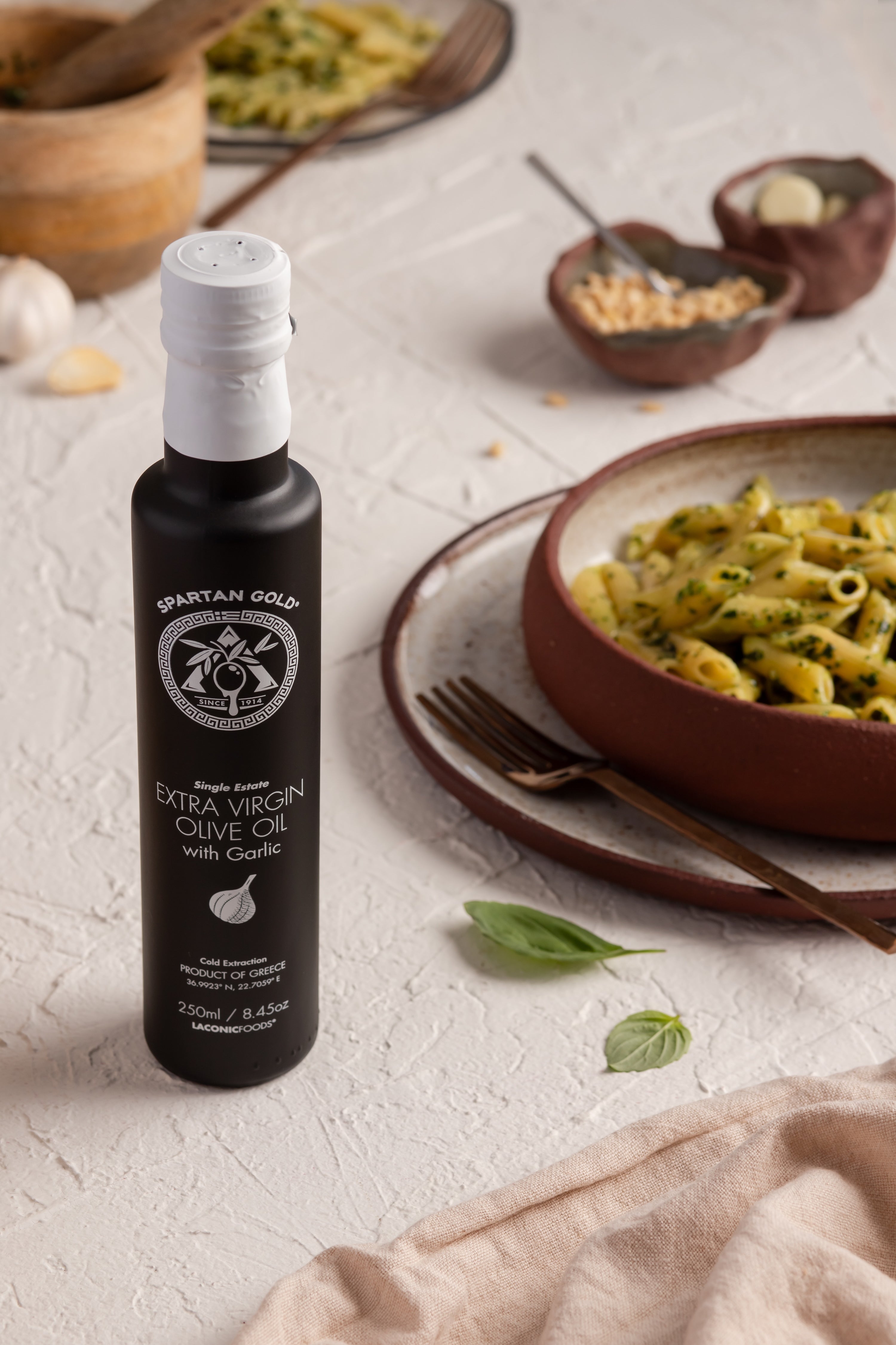 Garlic EVOO bottle next to a bowl of pasta with basil, showcasing Mediterranean cooking