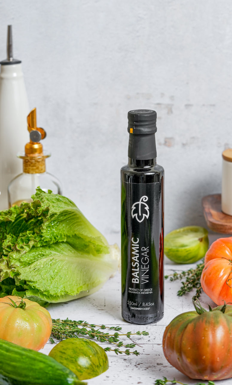 250ml bottle of Laconic Foods Balsamic Vinegar from Kalamata with lettuce, herbs, and tomatoes