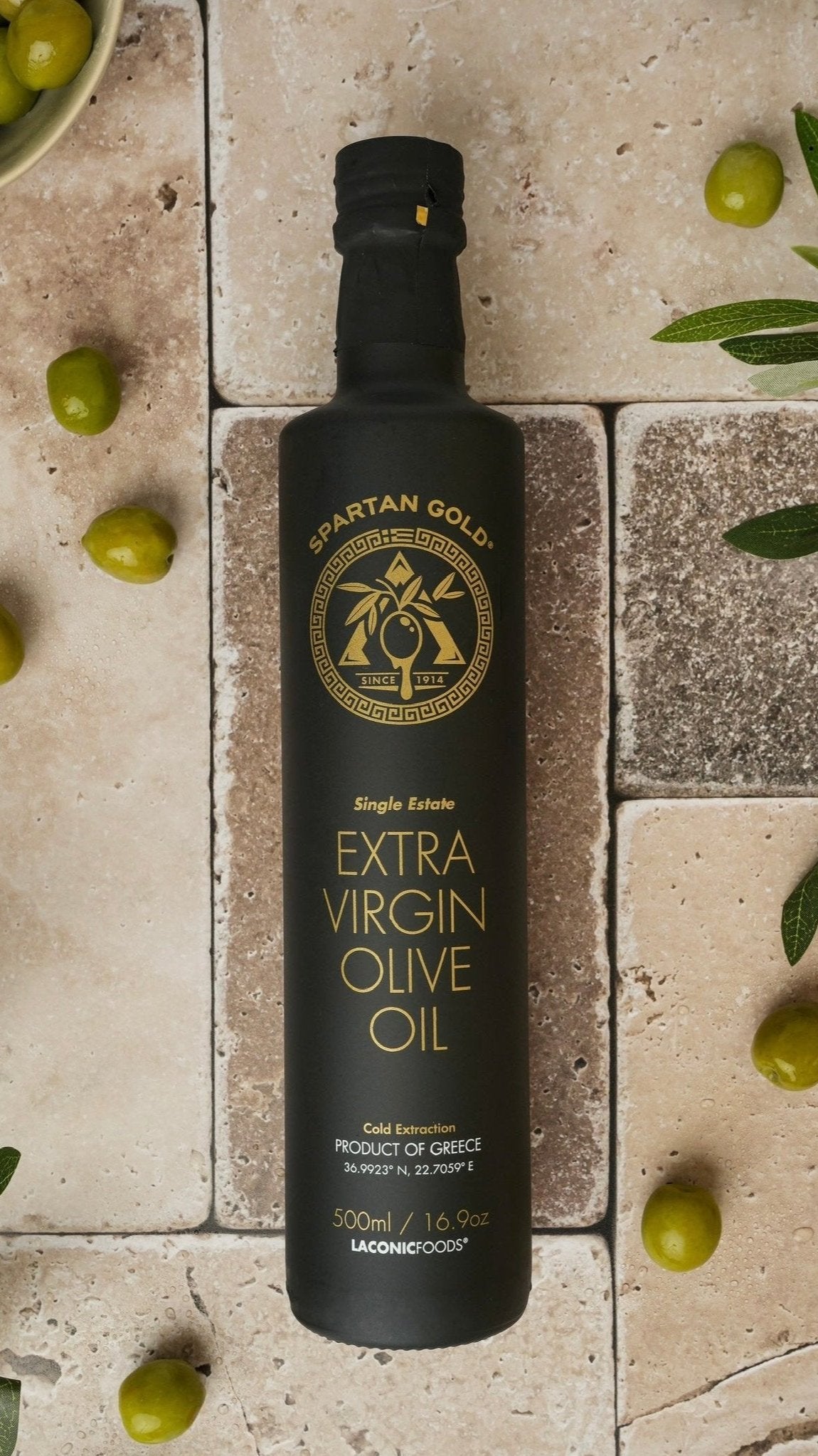 Laconic Foods Extra Virgin Olive Oil 500ml with fresh green olives on rustic stone tiles