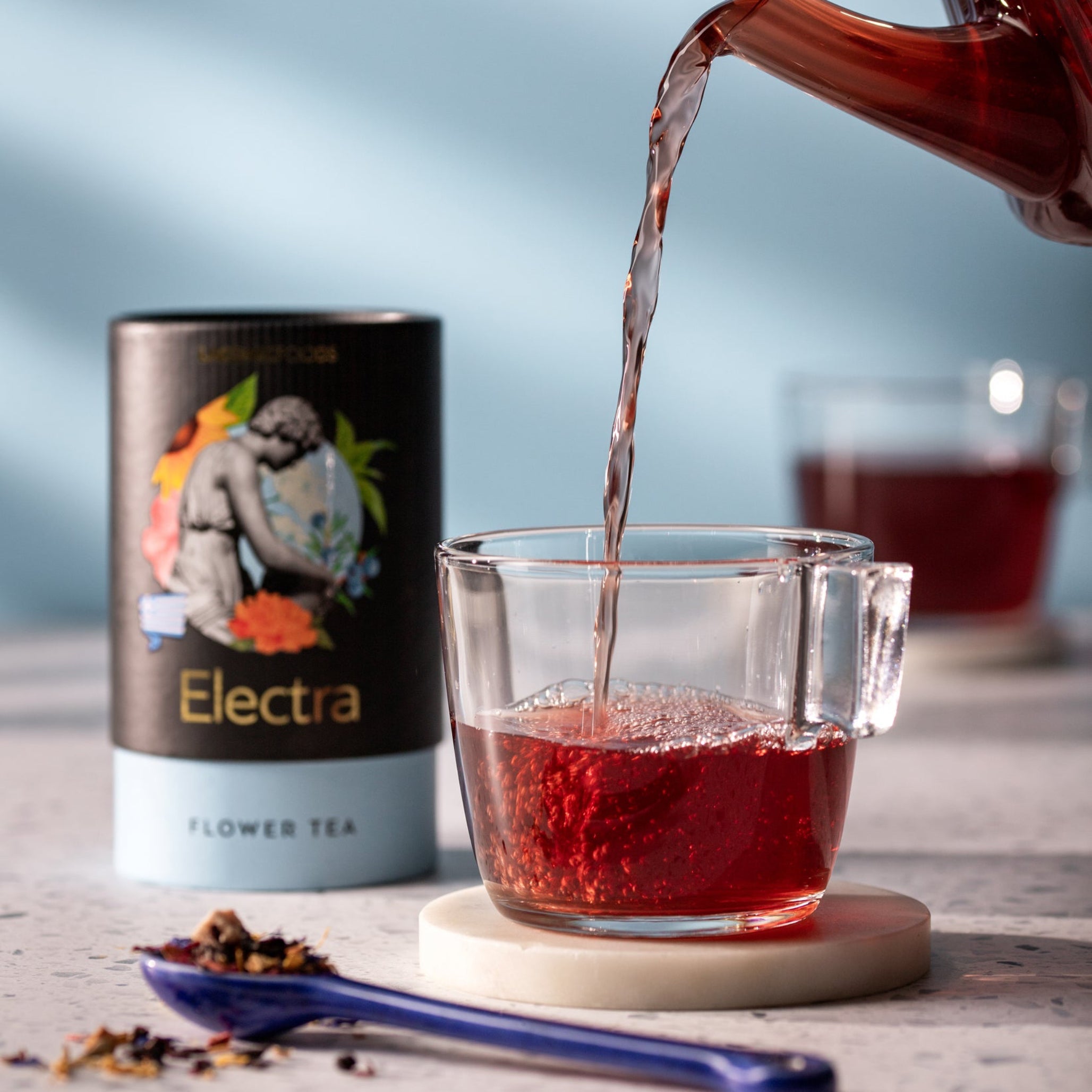 Laconic Foods Electra Flower Tea poured into glass cup with vivid red infusion – elegant Greek loose leaf tea with floral aroma.