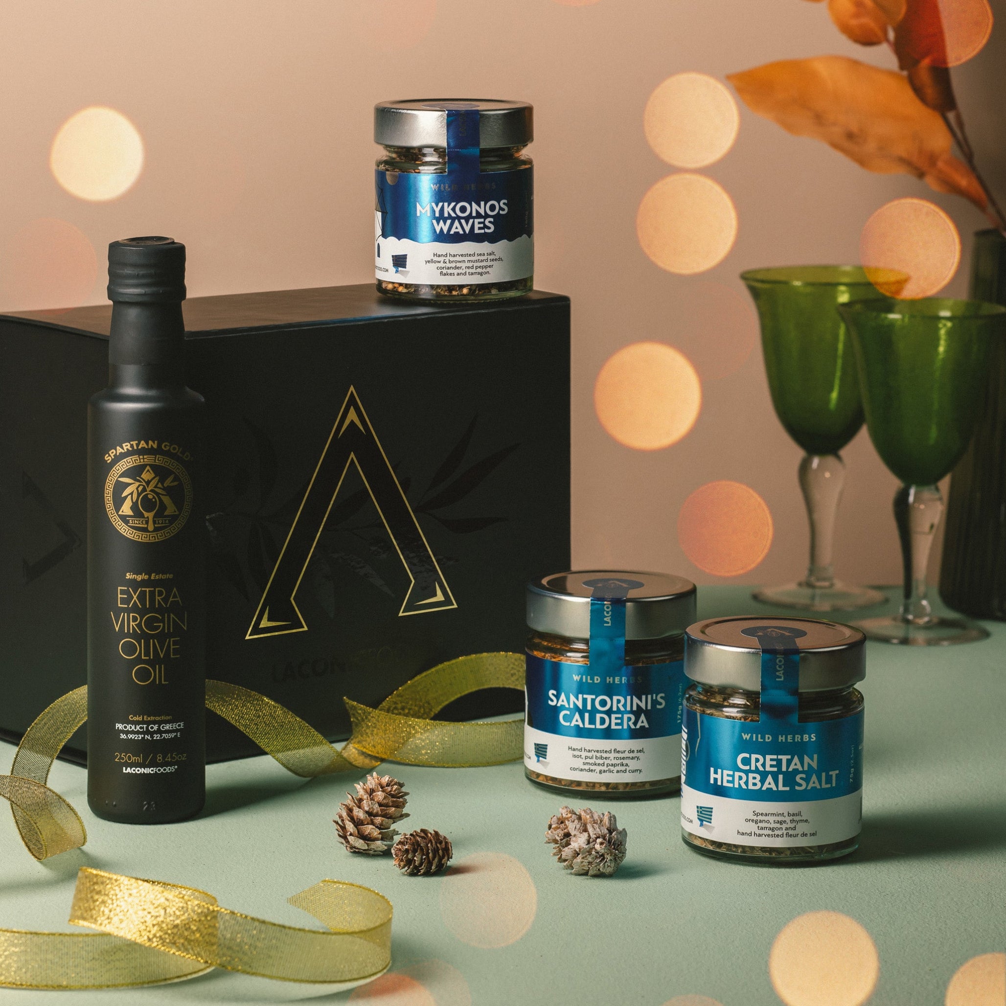 Festive holiday display of Laconic Foods Greek gift box with extra virgin olive oil and three herbal spice blends, styled with ribbon and pinecones.