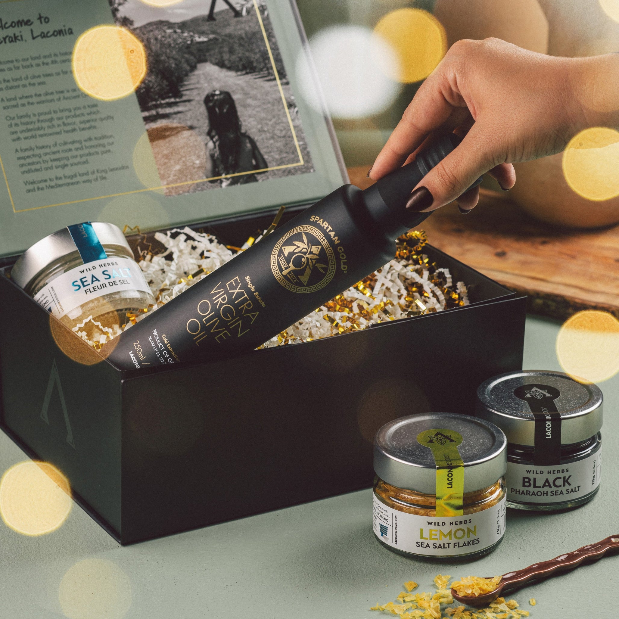 Laconic Foods luxury Greek gift set – hand holding extra virgin olive oil bottle with lemon, fleur de sel, and black sea salts