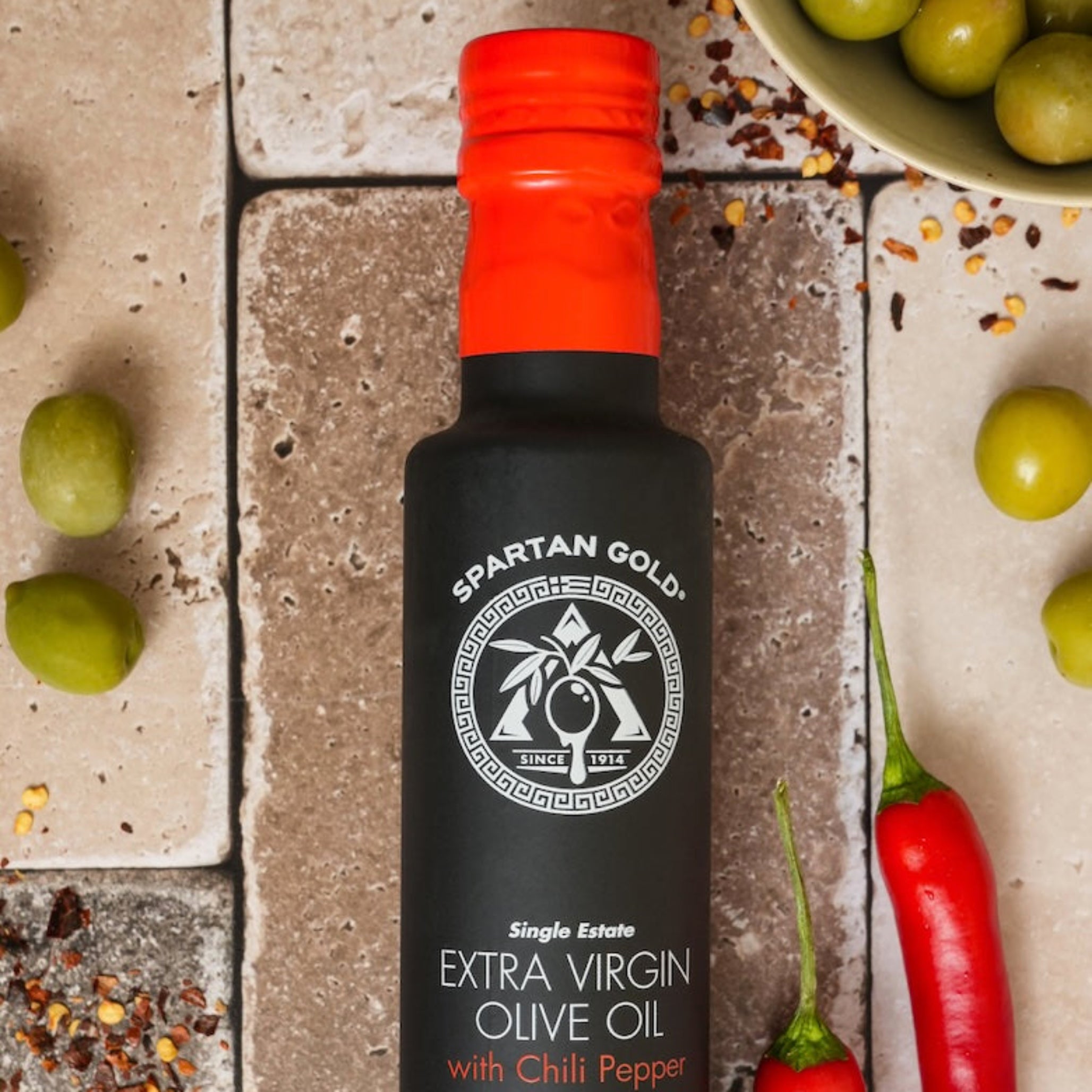Overhead shot of chili olive oil bottle with red chili peppers, crushed chili flakes, and green olives