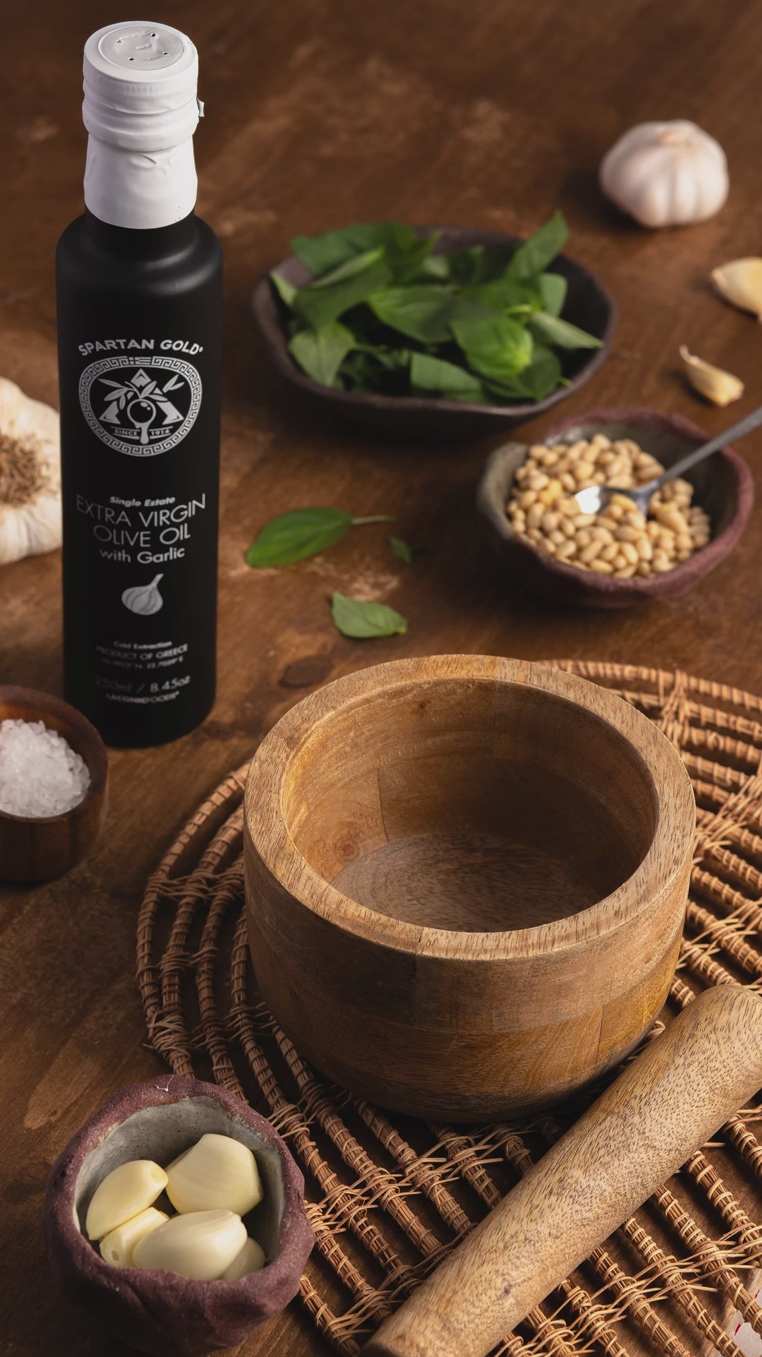 Mixing Laconic Foods Garlic EVOO with pine nuts, garlic cloves, sea salt, and fresh basil in a small bowl – artisanal flavor preparation in action.