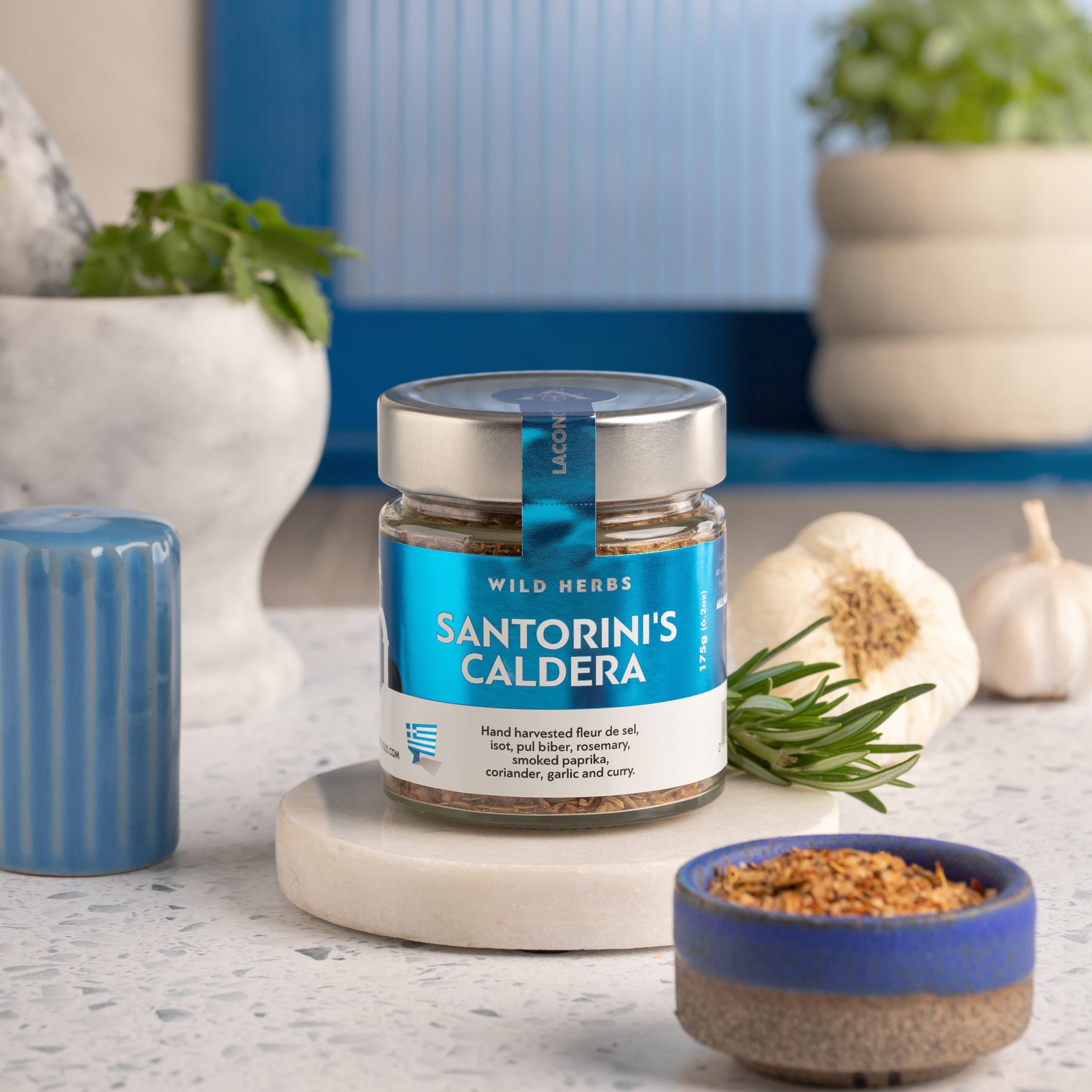 Santorini's Caldera spice jar styled on a countertop with rosemary, garlic, and a marble mortar – Mediterranean kitchen background