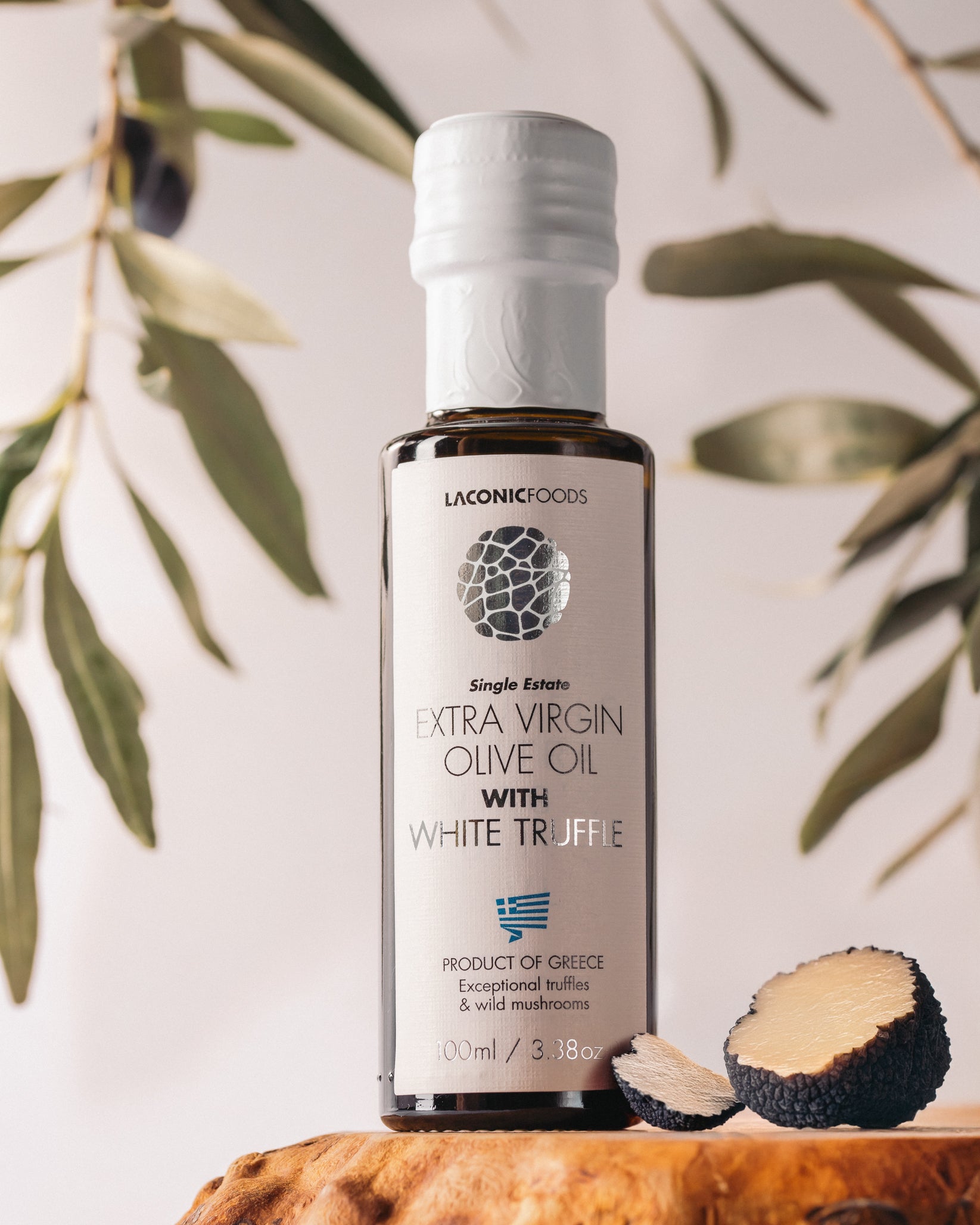 Laconic Foods Extra Virgin Olive Oil with White Truffle displayed with sliced truffles and olive branches.