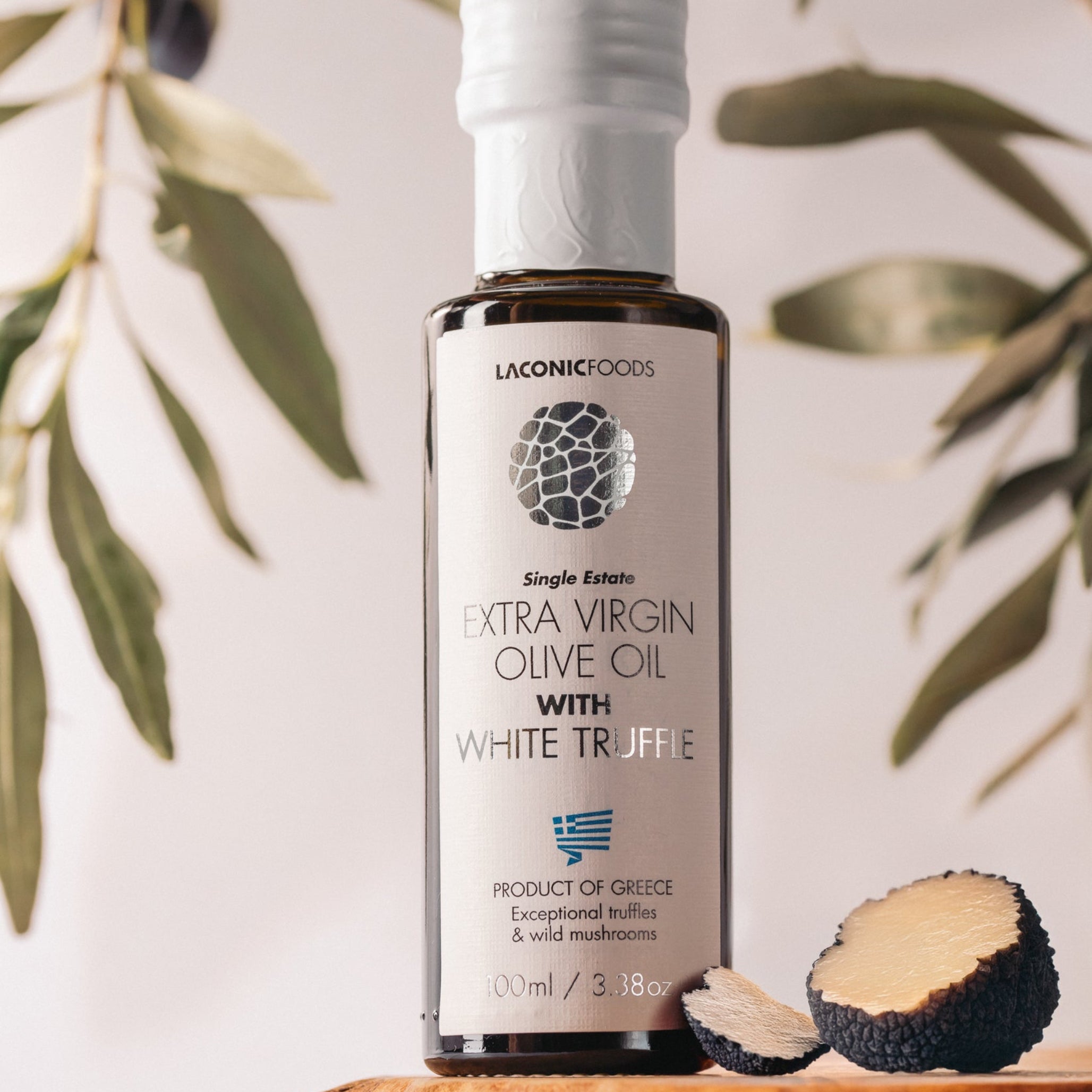 Laconic Foods Extra Virgin Olive Oil with White Truffle displayed with sliced truffles and olive branches.